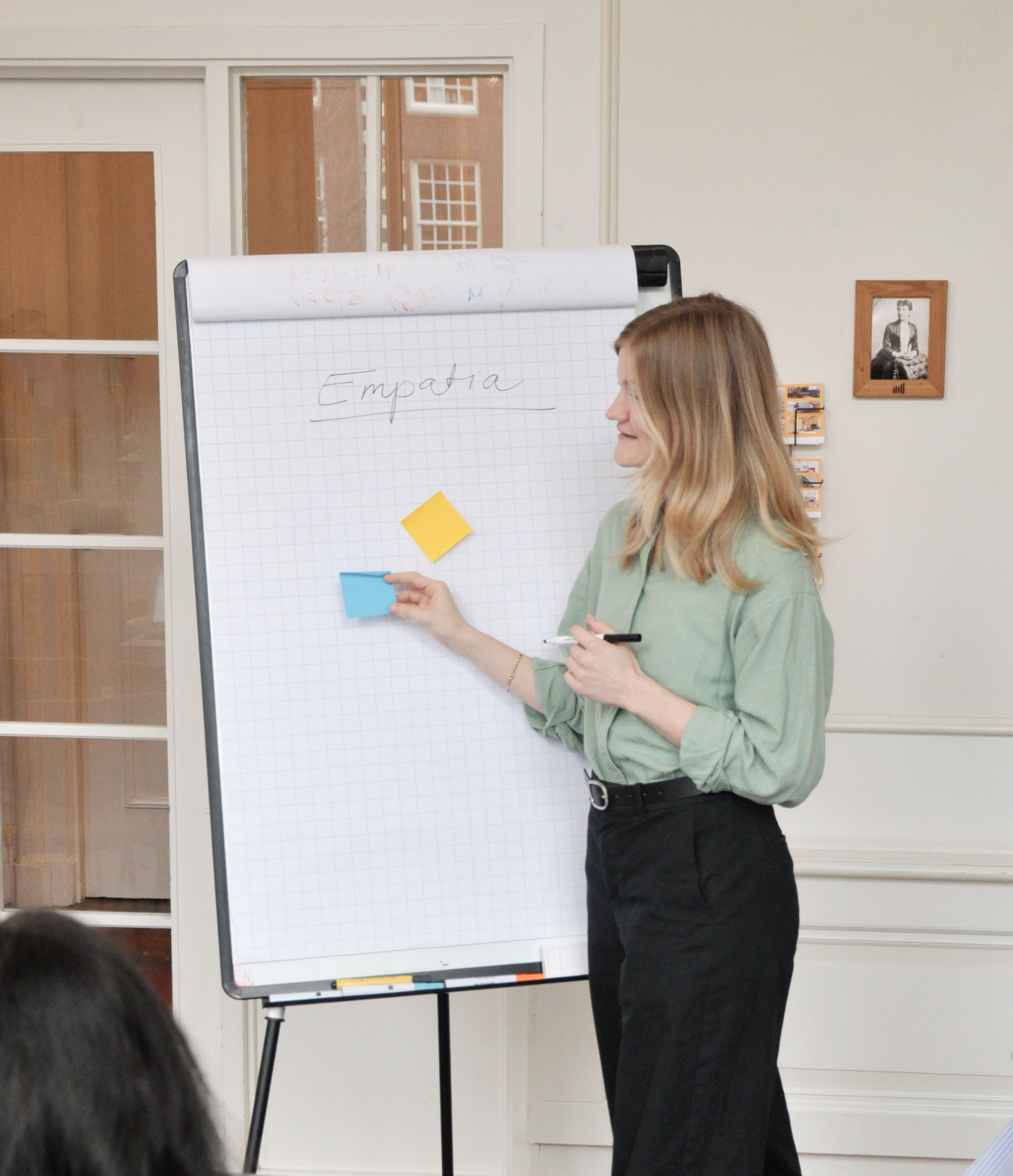 A woman standing at a flipchart labeled ‘Empatia,’ placing a sticky note, illustrating guidance on finding a Ukrainian-speaking psychotherapist.