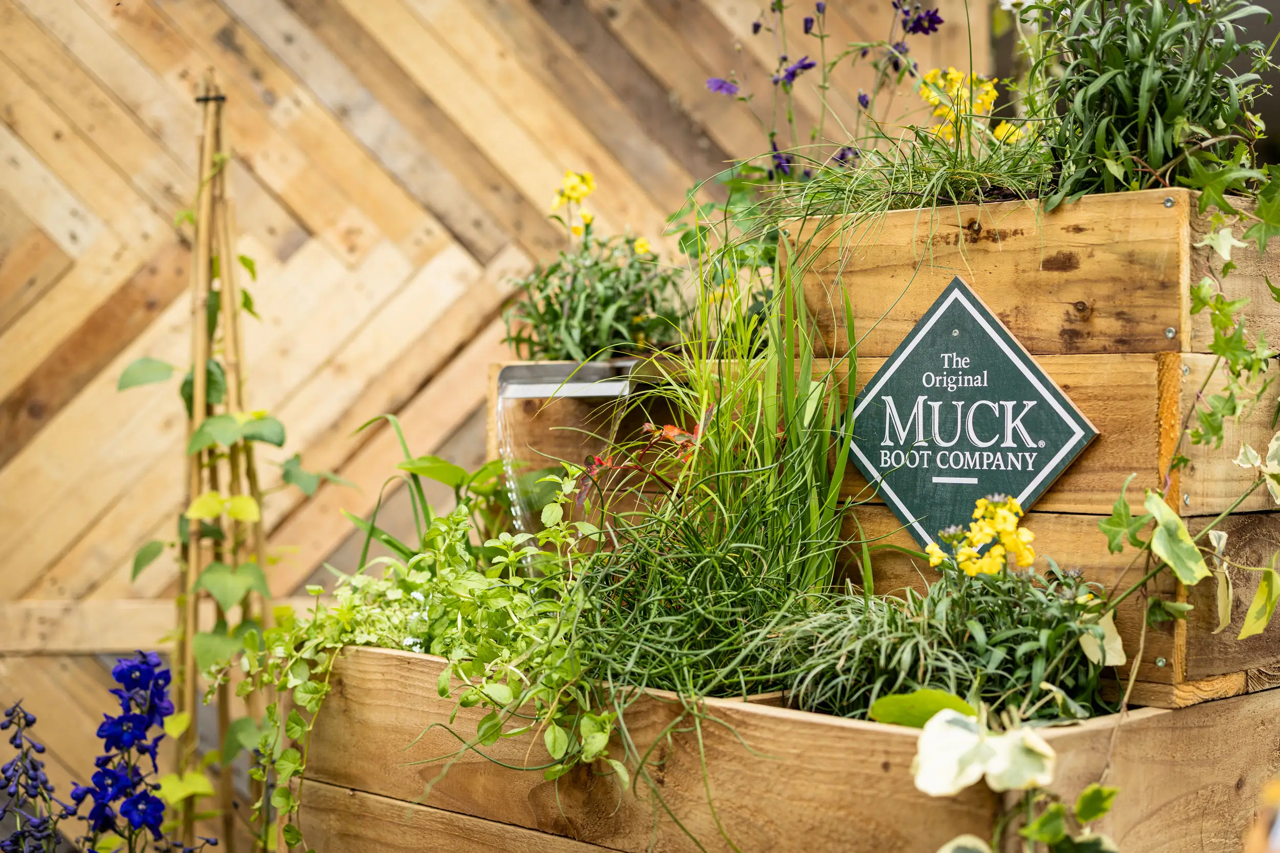 A lush vertical garden featuring various plants, herbs, and flowers against a wooden backdrop and decorative sign.