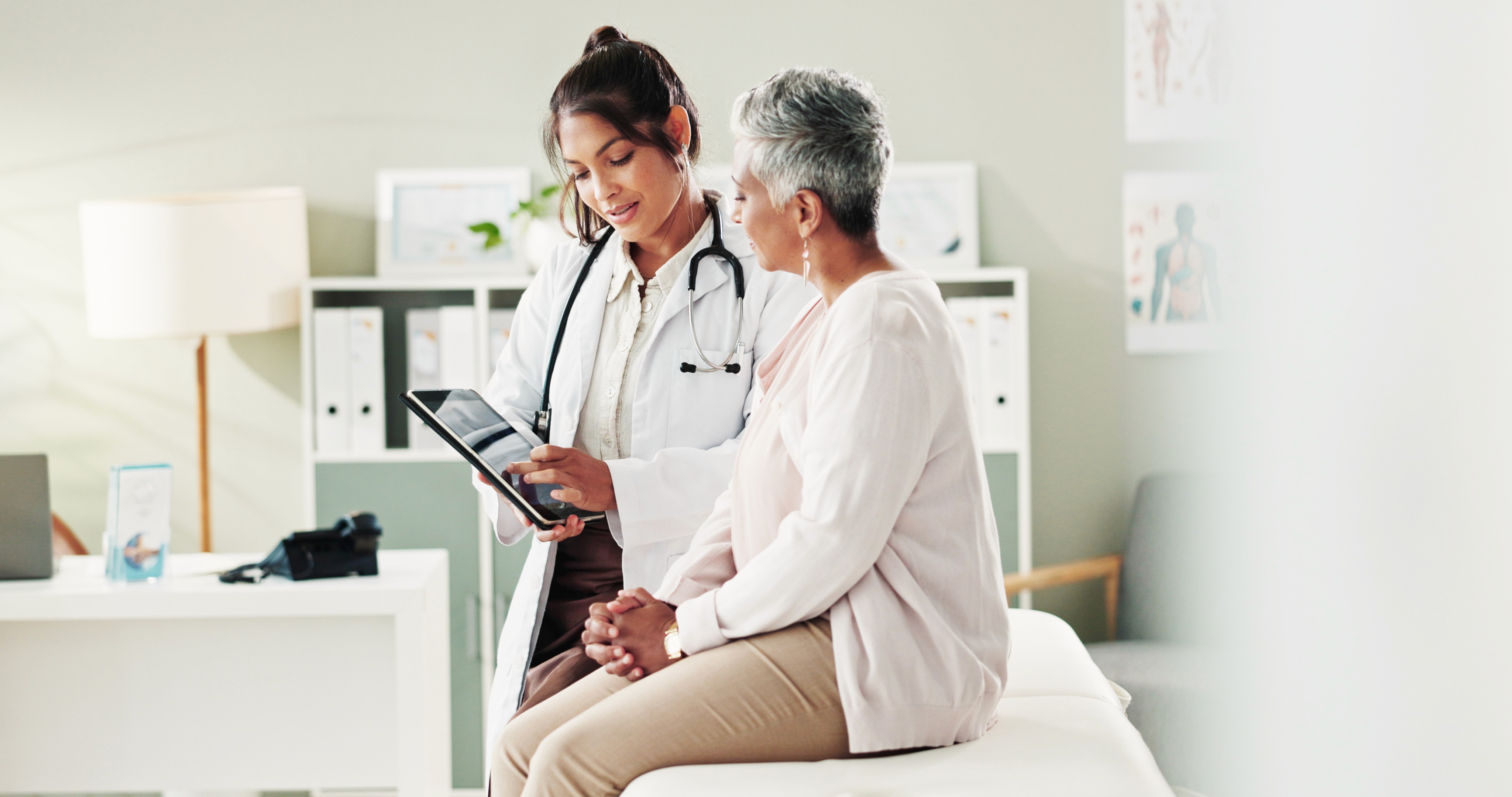 EHS client seats on a doctors bed while a GP shows her something on a surface pro
