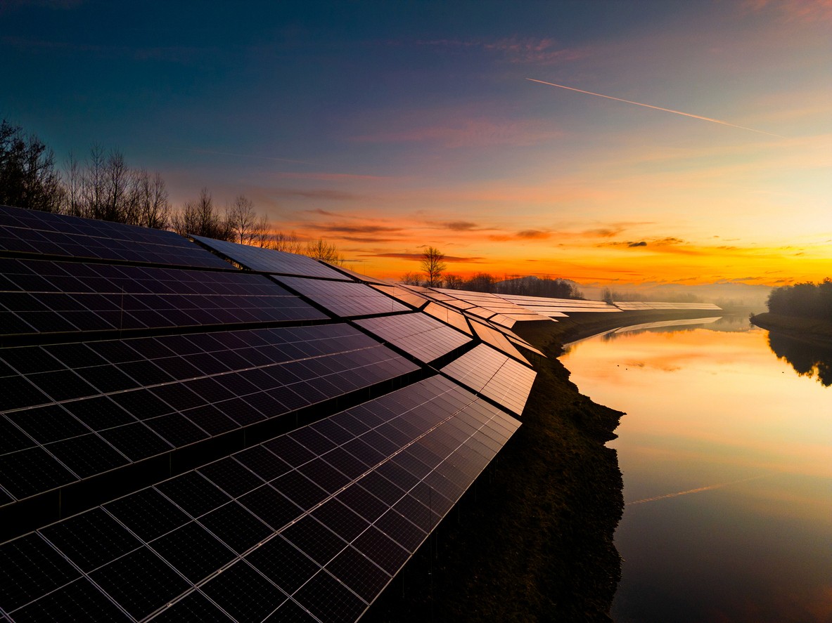solar panel farm along a river as the sun sets in the distance