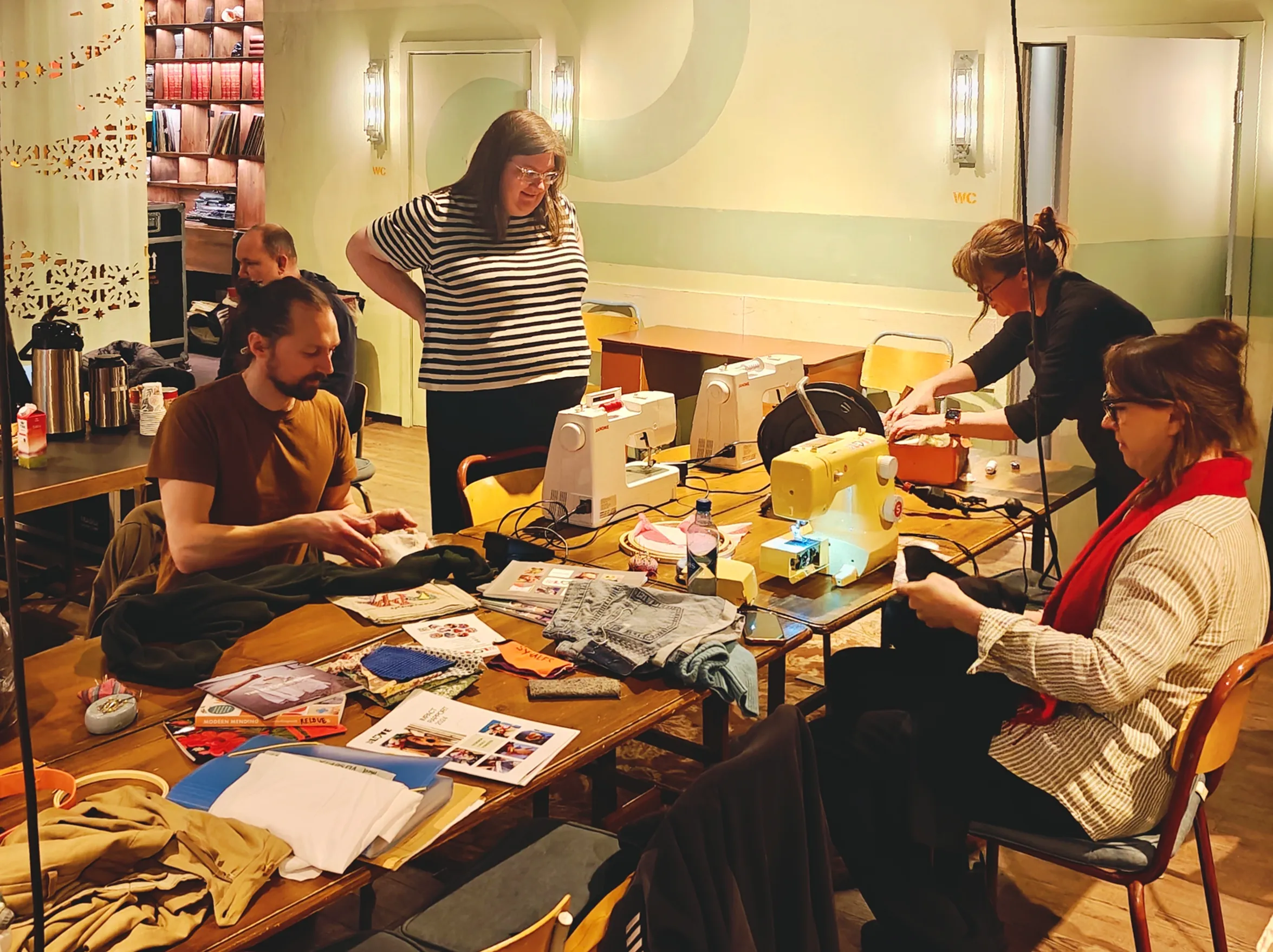 People sitting around a desk with sewing machines, mending clothes