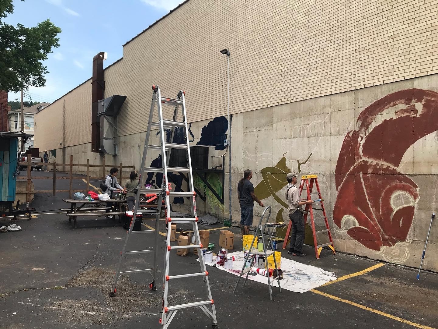 Ladders and drop cloths along the wall as the first rust-red shapes and dark figures appear.