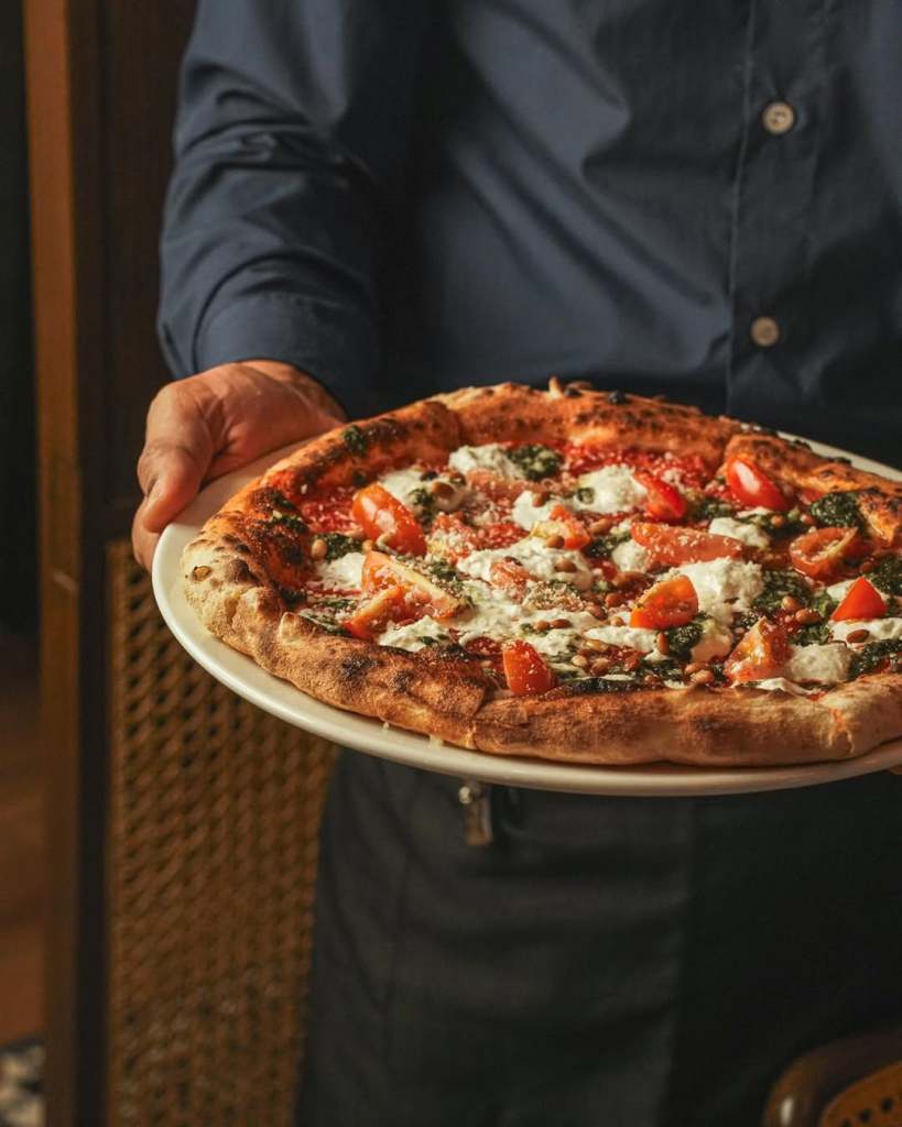 A person holding a plate of pizza topped with tomatoes, cheese, and herbs, presenting it with pride.