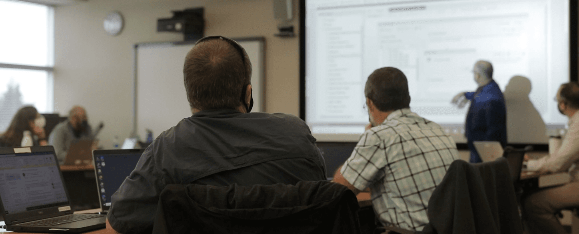 A classroom training session with participants seated at laptops while an instructor presents information on a projector screen—representing in-person technical or cybersecurity training.