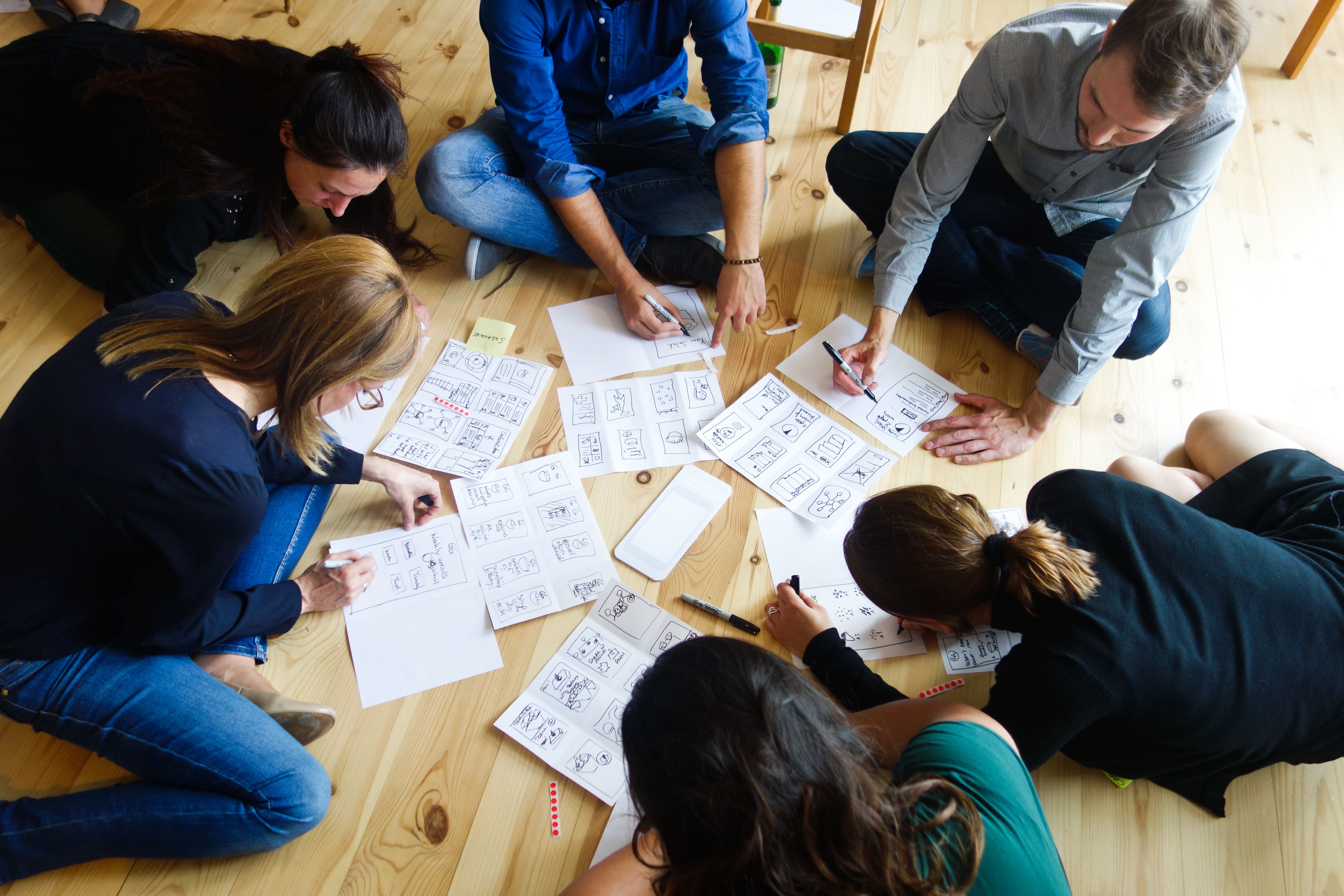 Workshop participants sketching storyboard solutions together on a wooden floor during a design sprint