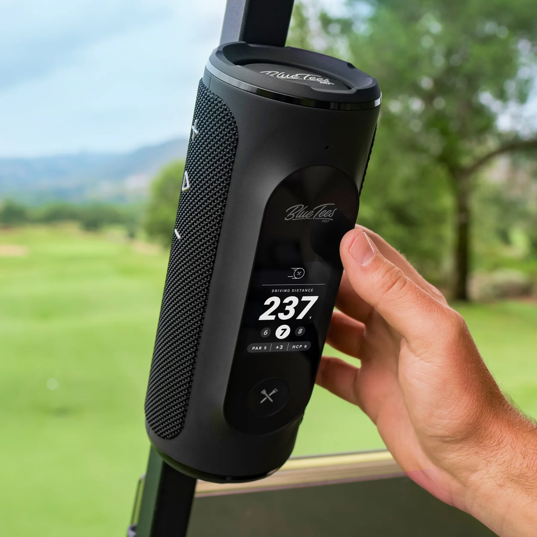 A Blue Tees Golf Player+ GPS Speaker on rail of a golf cart on a course.