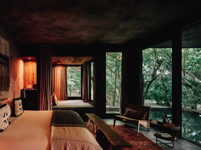 Fuego Suite at Nômade Tulum featuring luxurious finishes and incredible design, comfortable bed with pillows and cushions, 2 hanging lamps in harmony, and huge windows with private pool view.