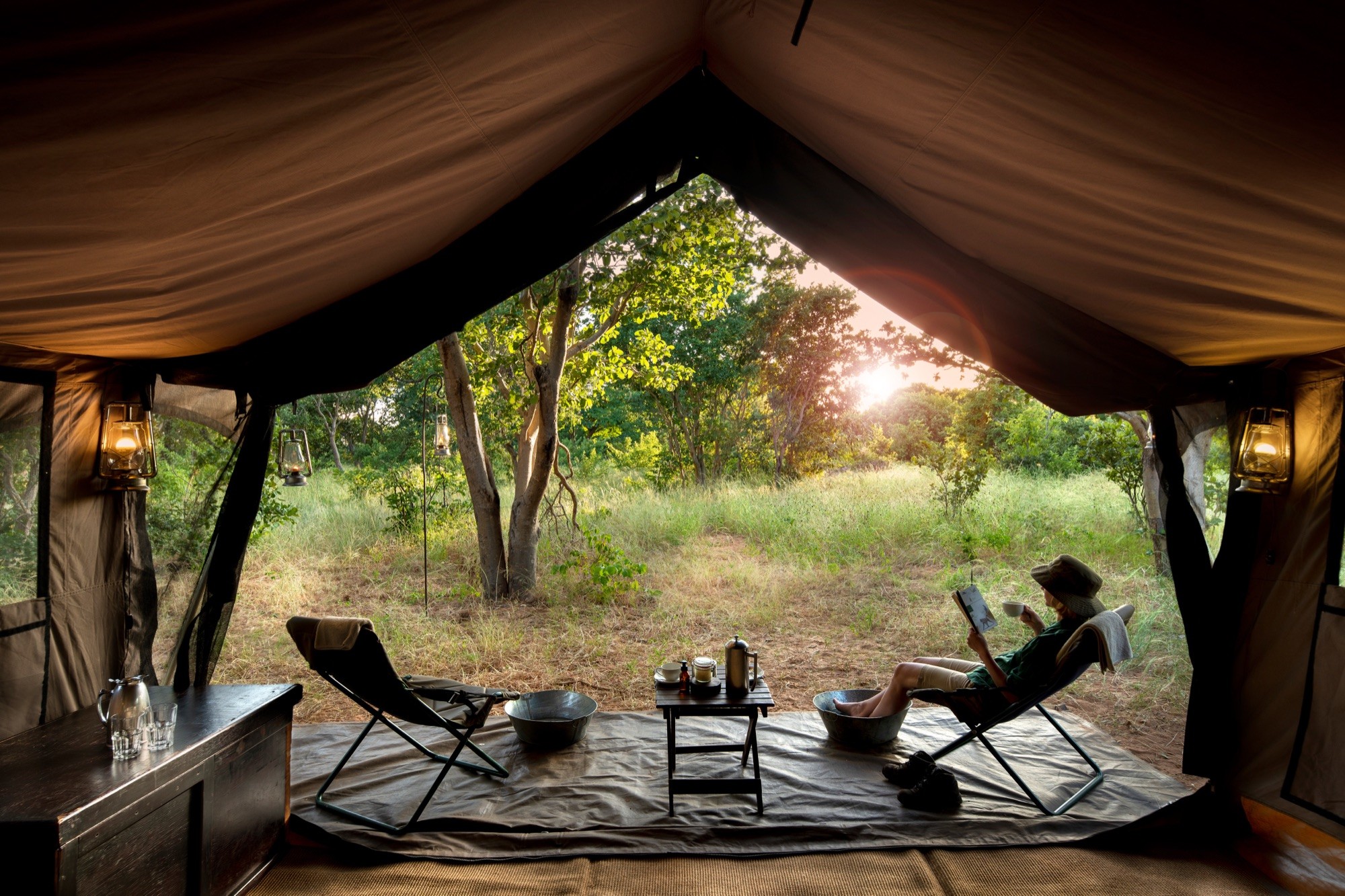A guest reading in a camp chair at the open flap of a canvas tent