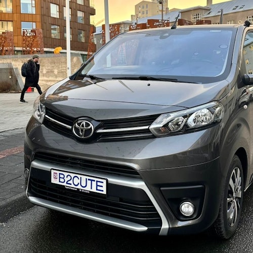 Un monovolumen Toyota gris con una matrícula personalizada "B2CUTE" estacionado en una calle de la ciudad. Se ve a un peatón al fondo.