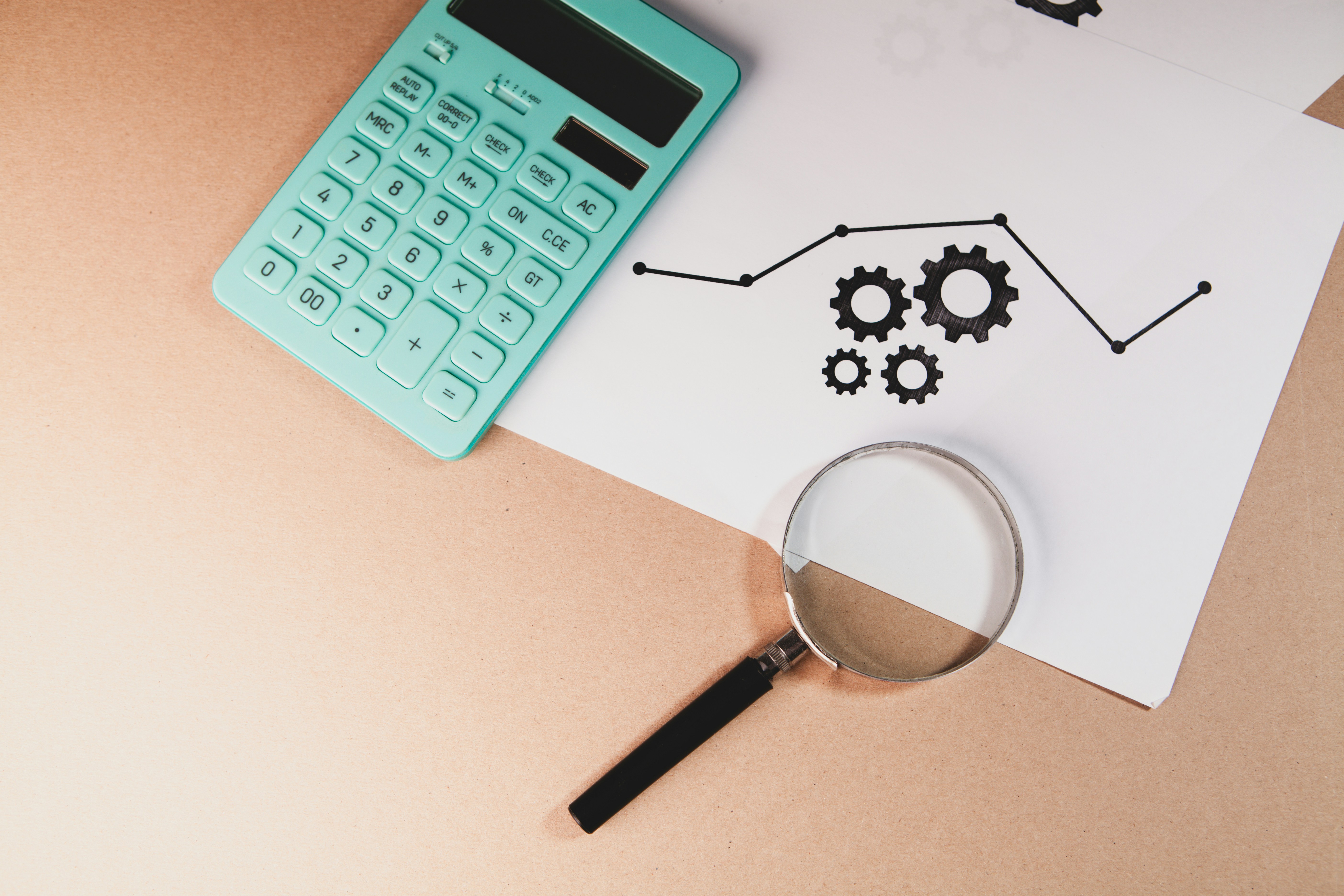 Calculator, magnifying glass, and chart with gears on paper.