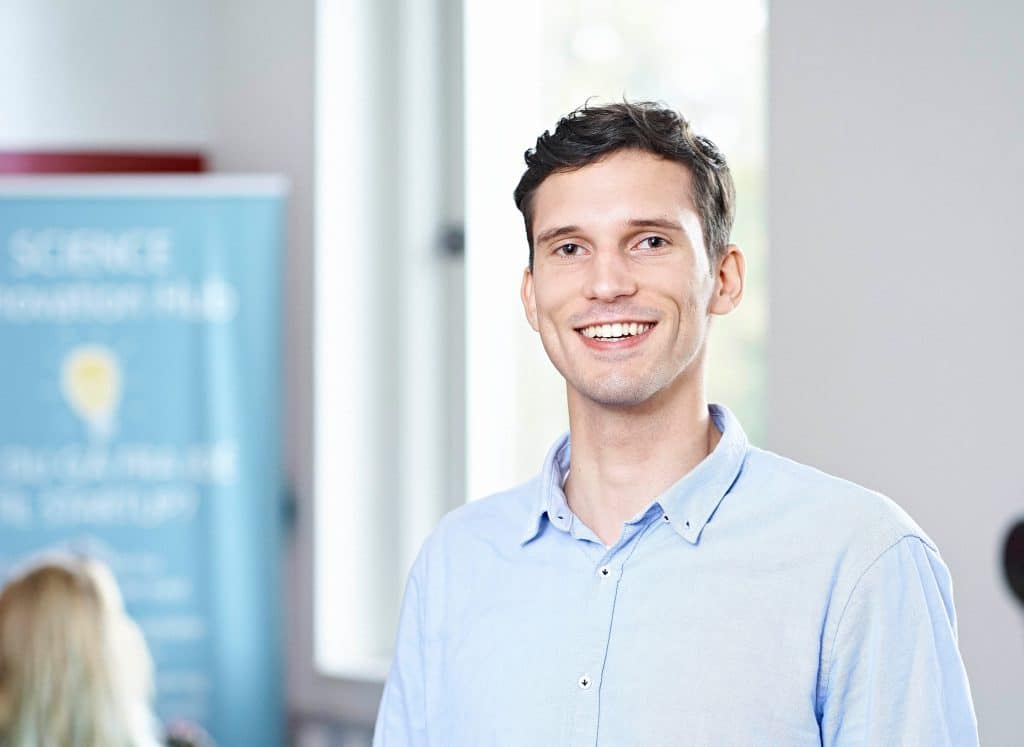 a white man with a blue collared shirt smiling into camera