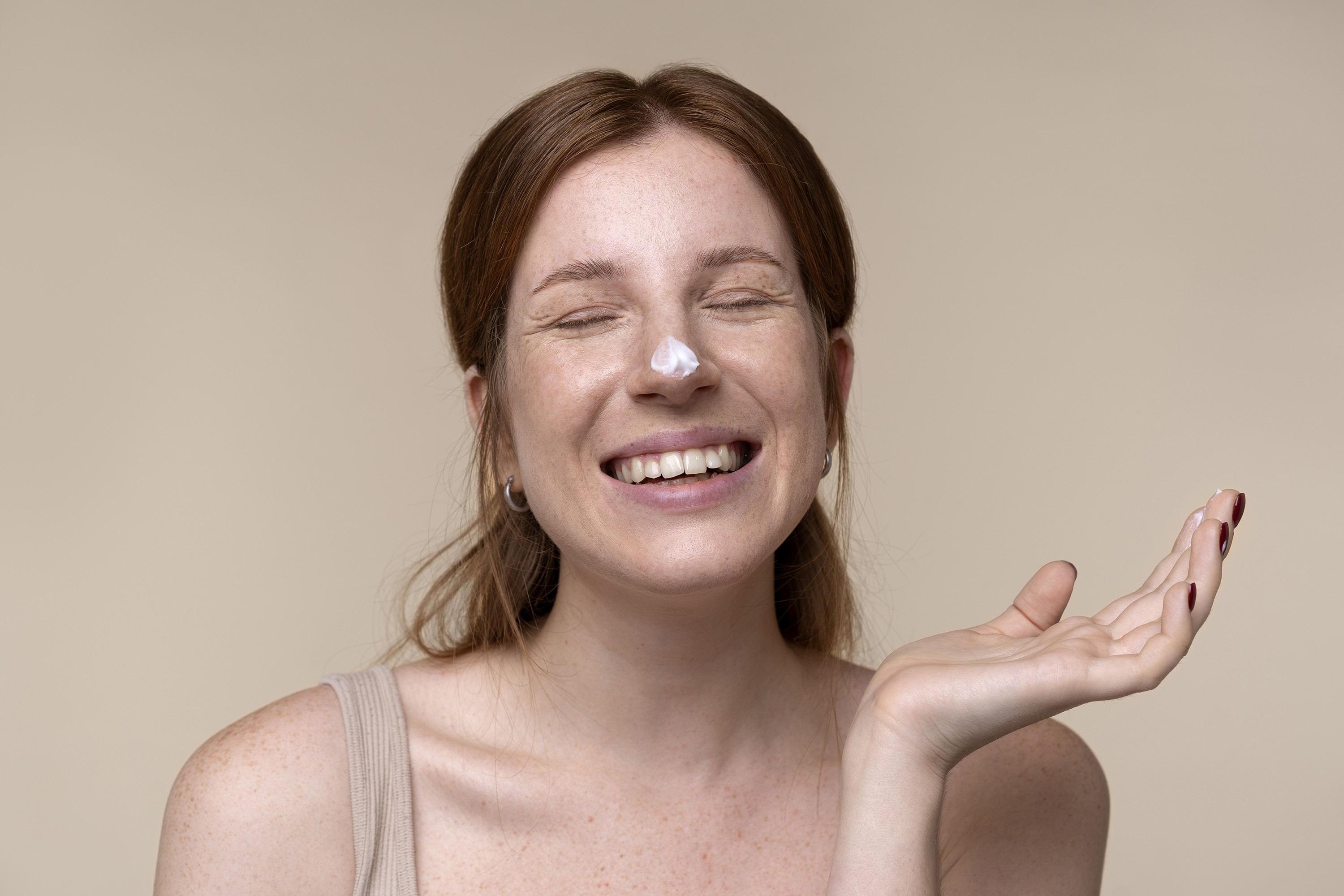 Smiling woman with a dab of moisturizer on her nose, eyes closed, enjoying her skincare routine