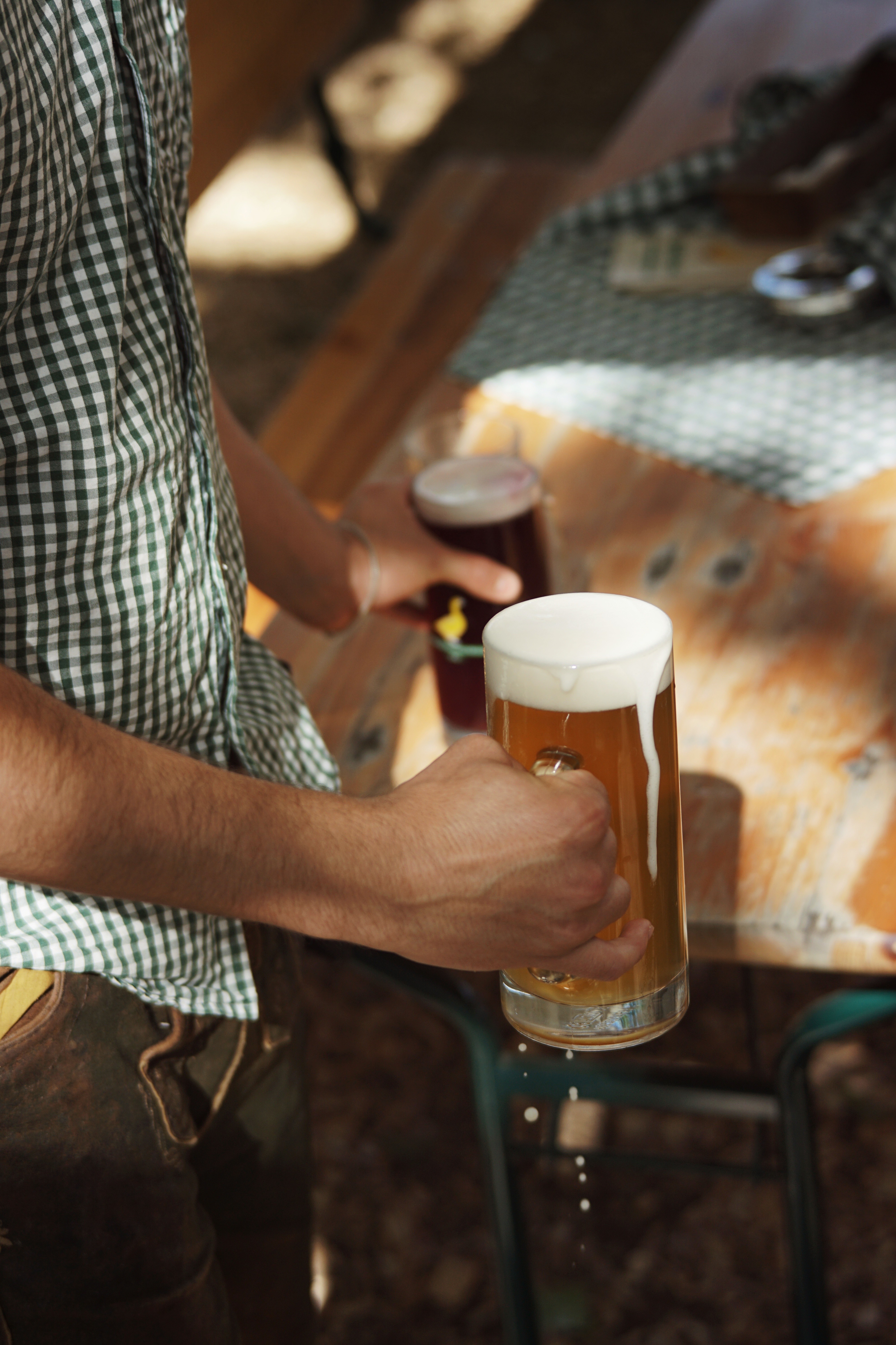 Person stellt ein helles und ein dunkles Bier ind Bierkrügen mit dem Logo "Goldene Gans" auf Biertisch