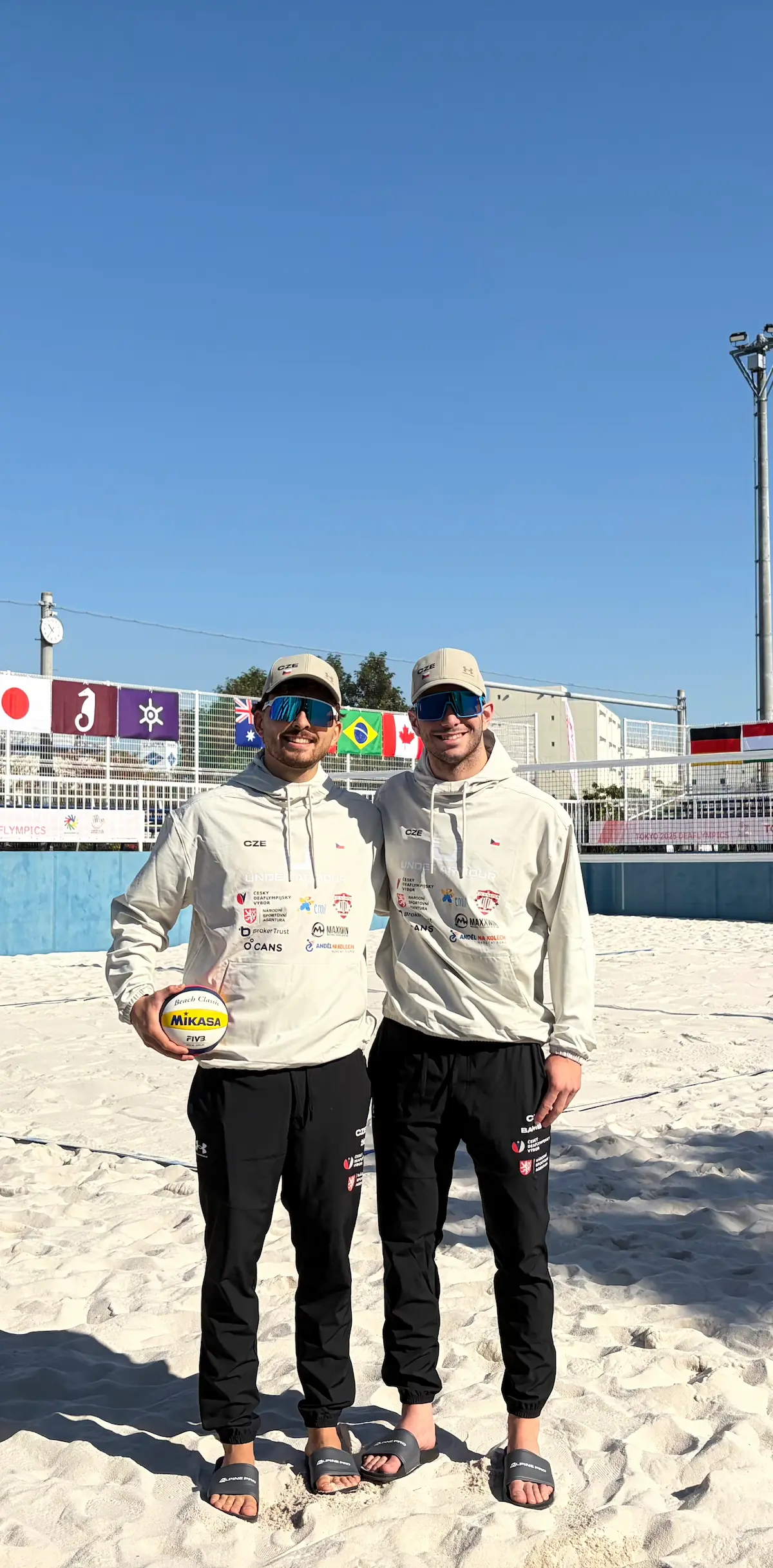 Jan Žídek a Šimon Bambas na beachvolejbalovém kurtu v Tokiu v reprezentační teplákové soupravě.