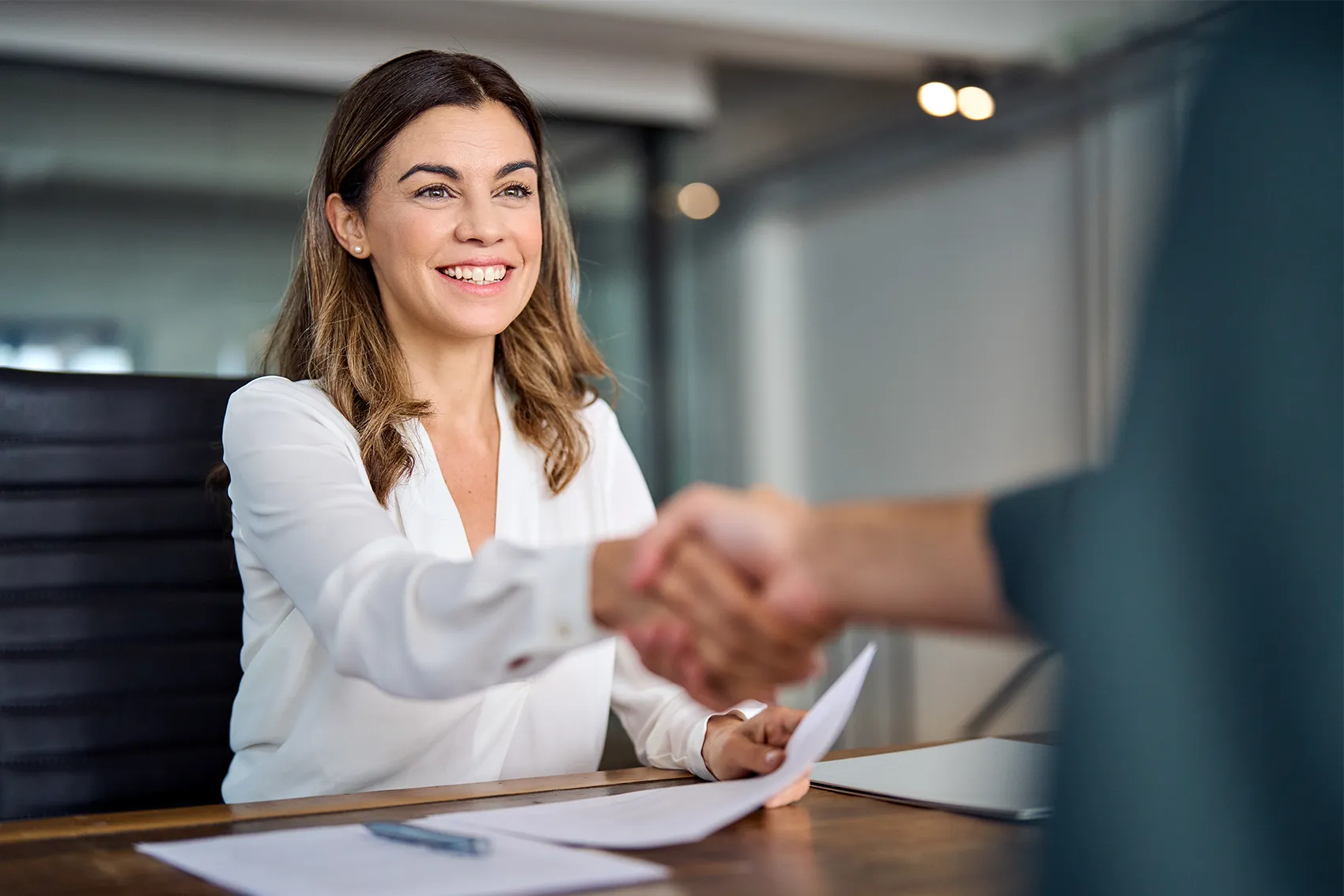 Am Schreibtisch sitzende Frau, die einer anderen Person die Hand schüttelt
