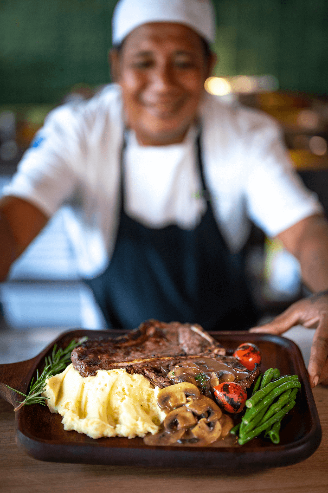 Plate of tender steak, mashed potatoes, green beans, and grilled vegetables being served by a chef.