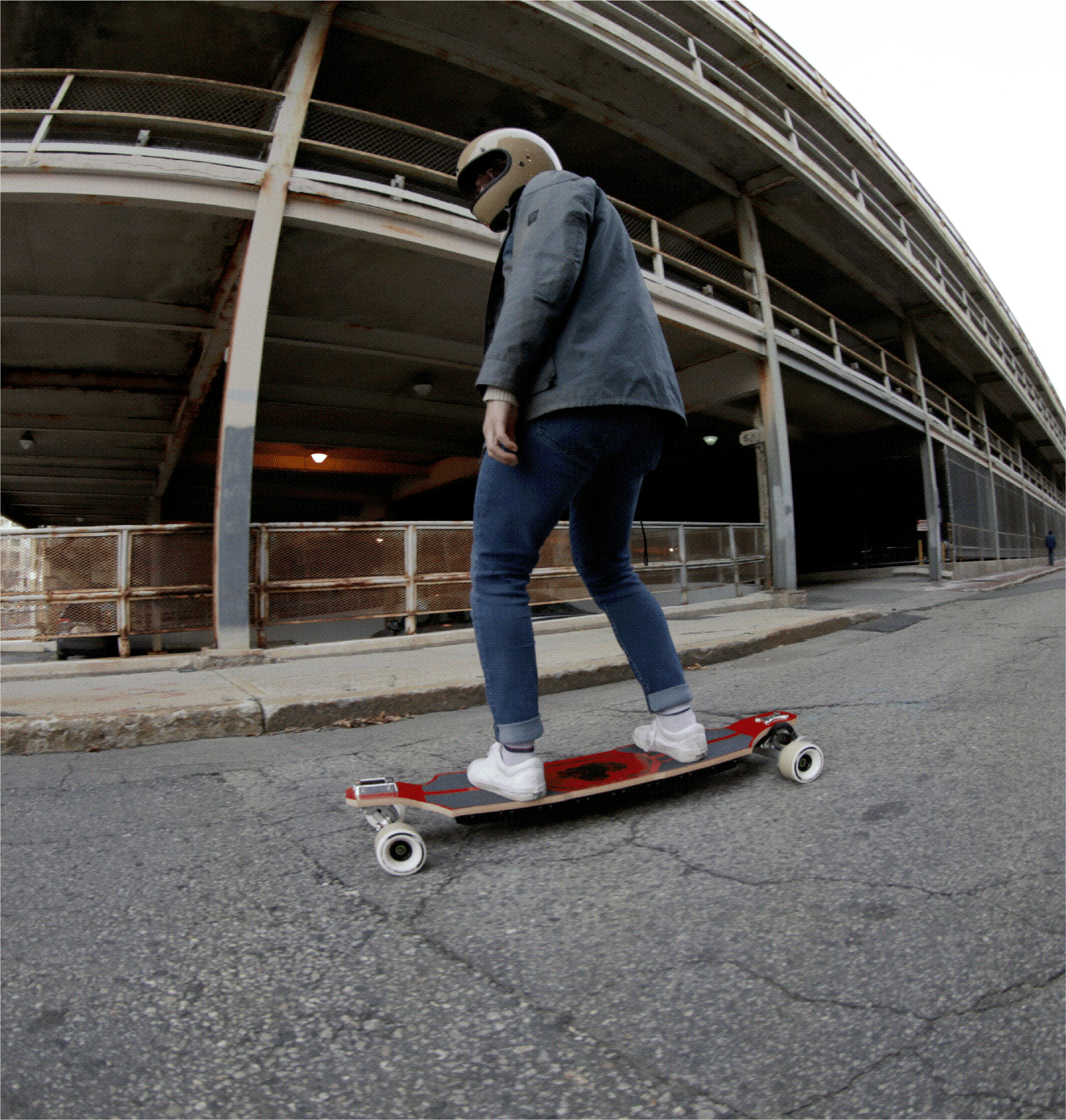 Person riding electric skateboard past a parking structure wearing helmet and casual clothing
