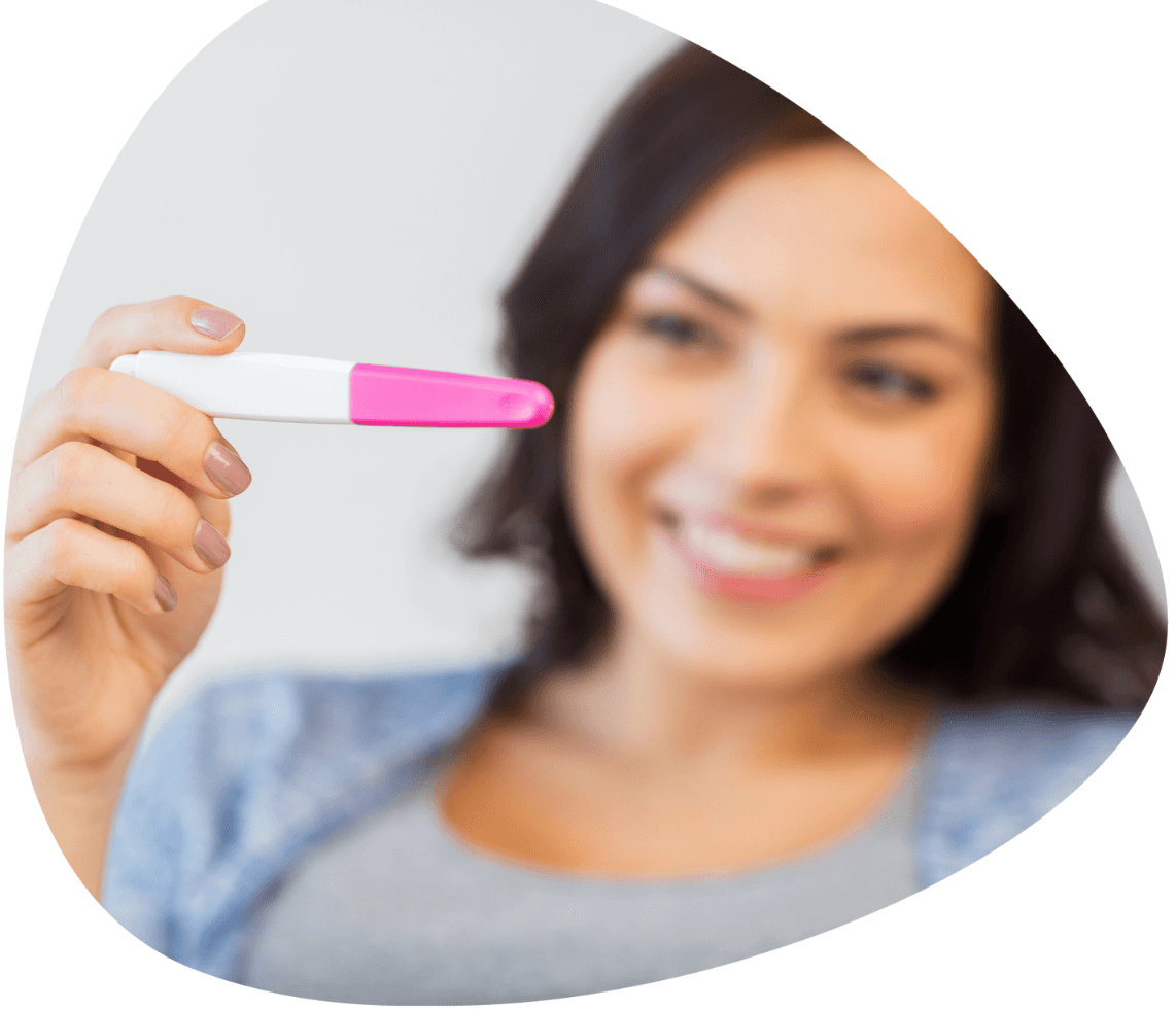 Smiling woman holding a positive pregnancy test, highlighting fertility health insurance benefits.