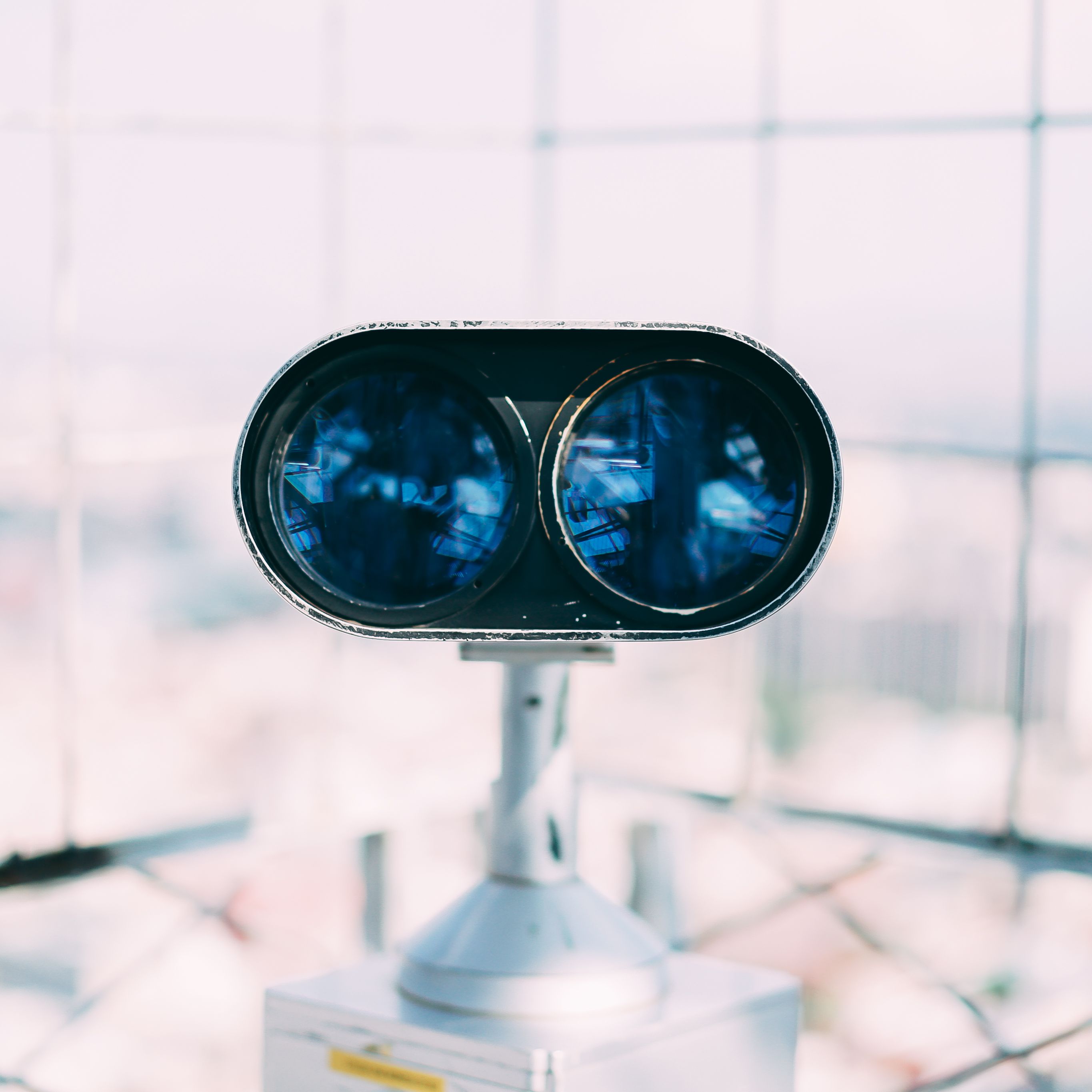 Close-up of blue tourist binoculars on an observation deck with a city view.