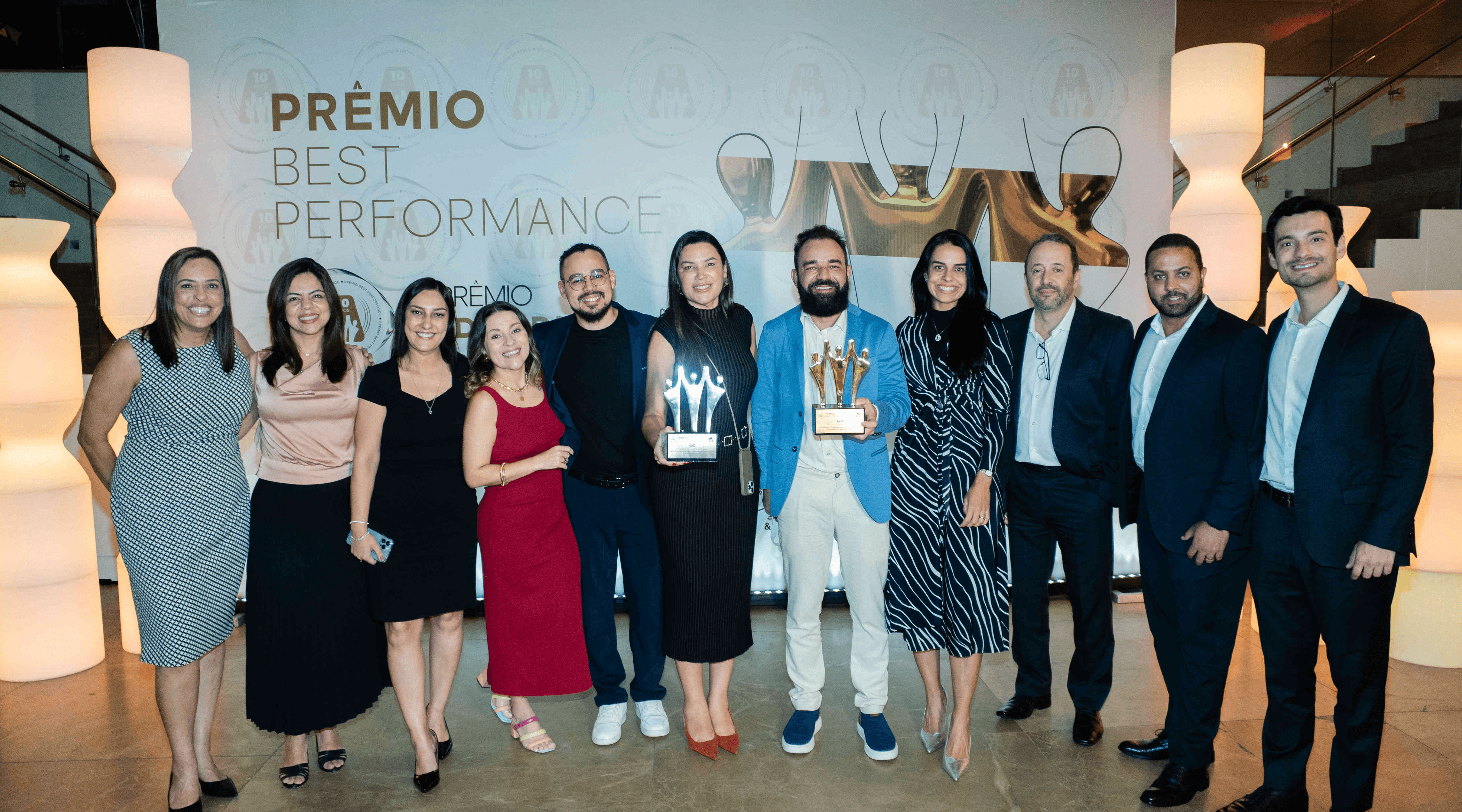 Executivos da AeC posando com troféu ouro e certificado no palco do Prêmio Best Performance 2025
