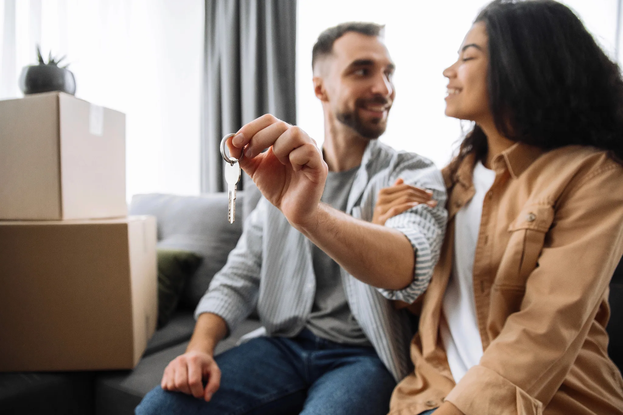 Smiling couple looking at each other, with the man holding house keys out in front of them.