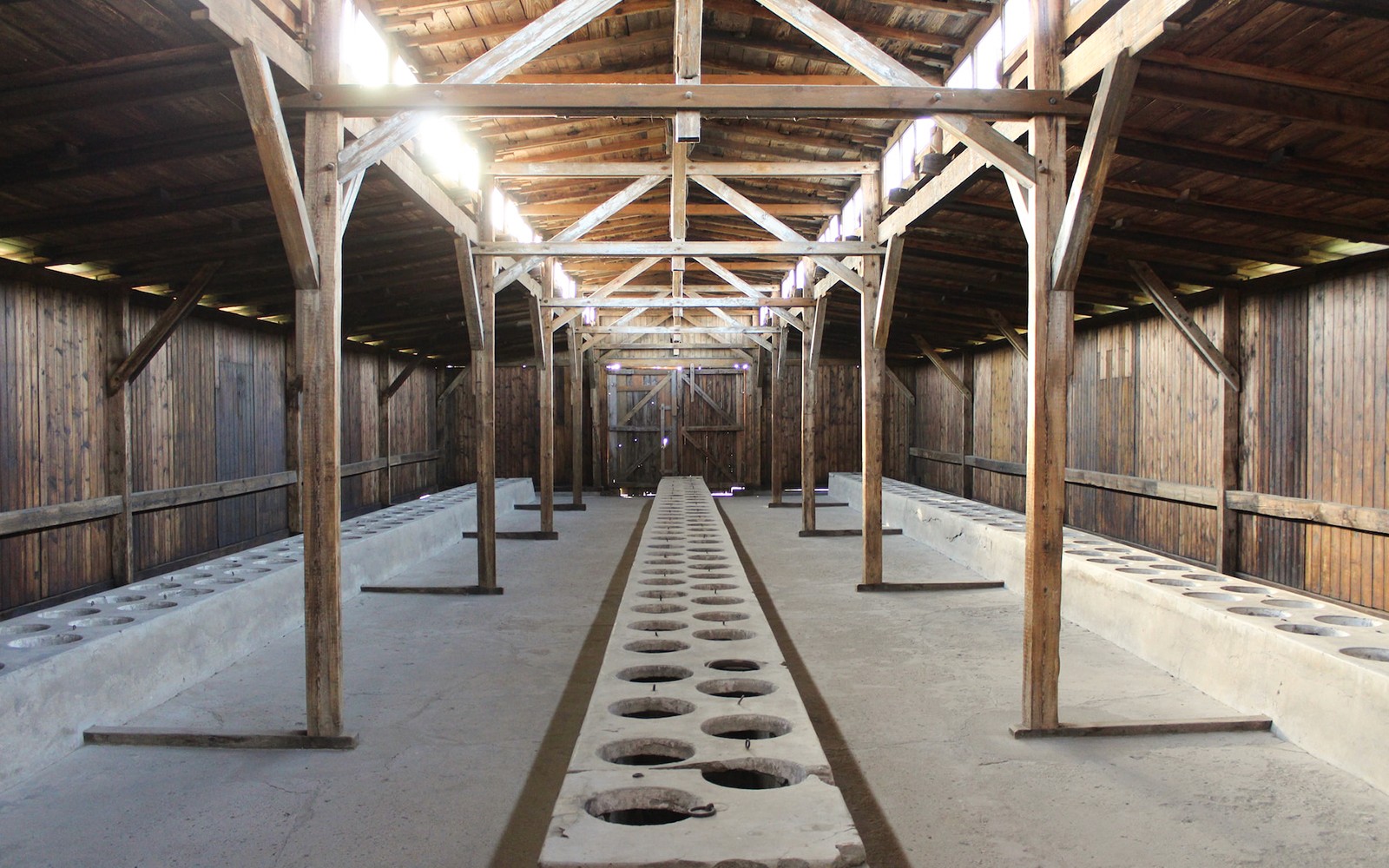 Innrétting í Auschwitz I-búðum sem sýnir viðarbeinagrindur og steinsteypta latrínur.
