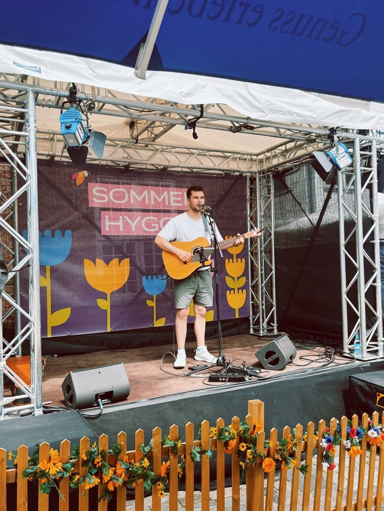 Ein Solomusiker steht auf einer kleinen Festivalbühne im Freien und spielt Gitarre.