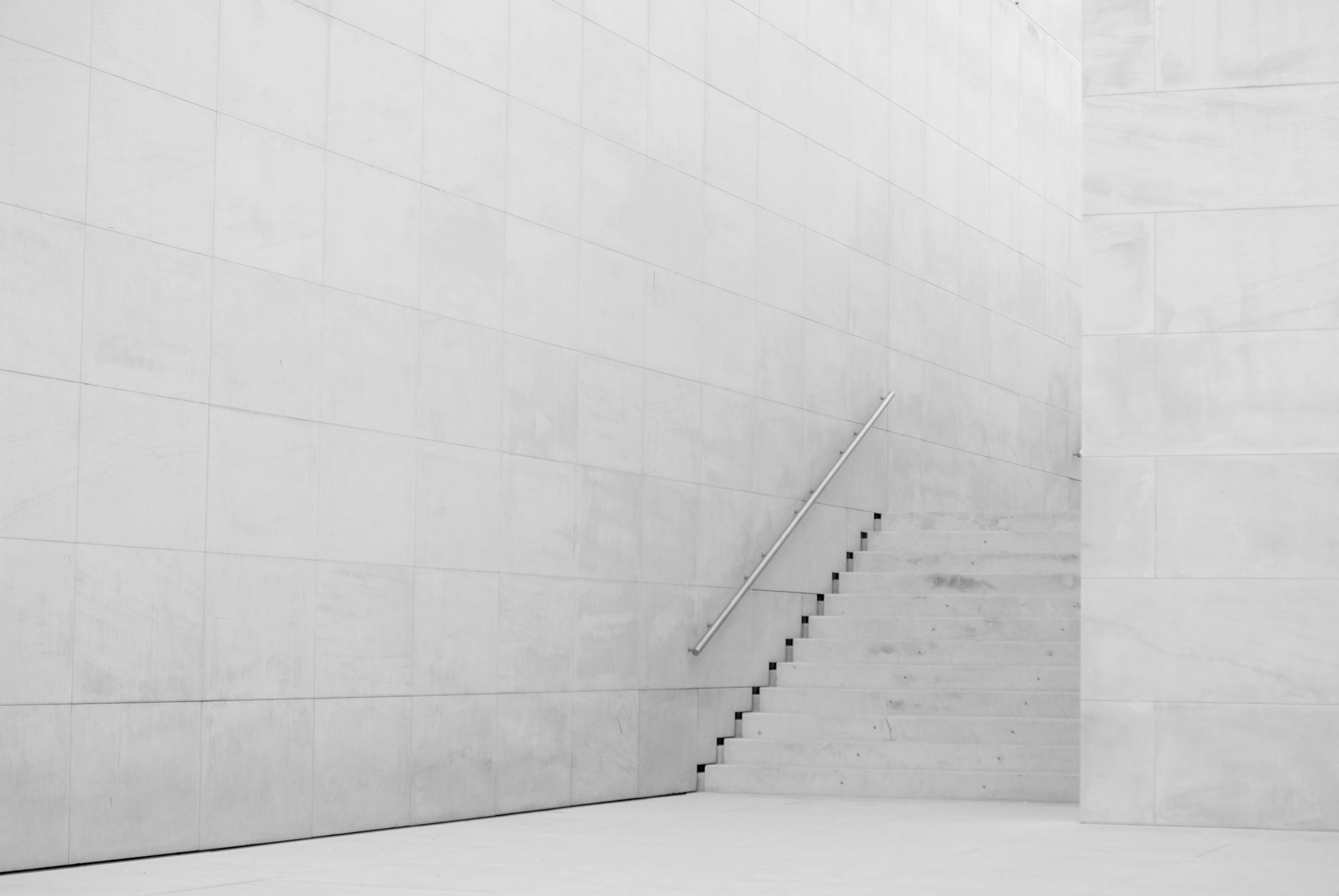A slender stair climbing a pale stone wall in a double-height hall