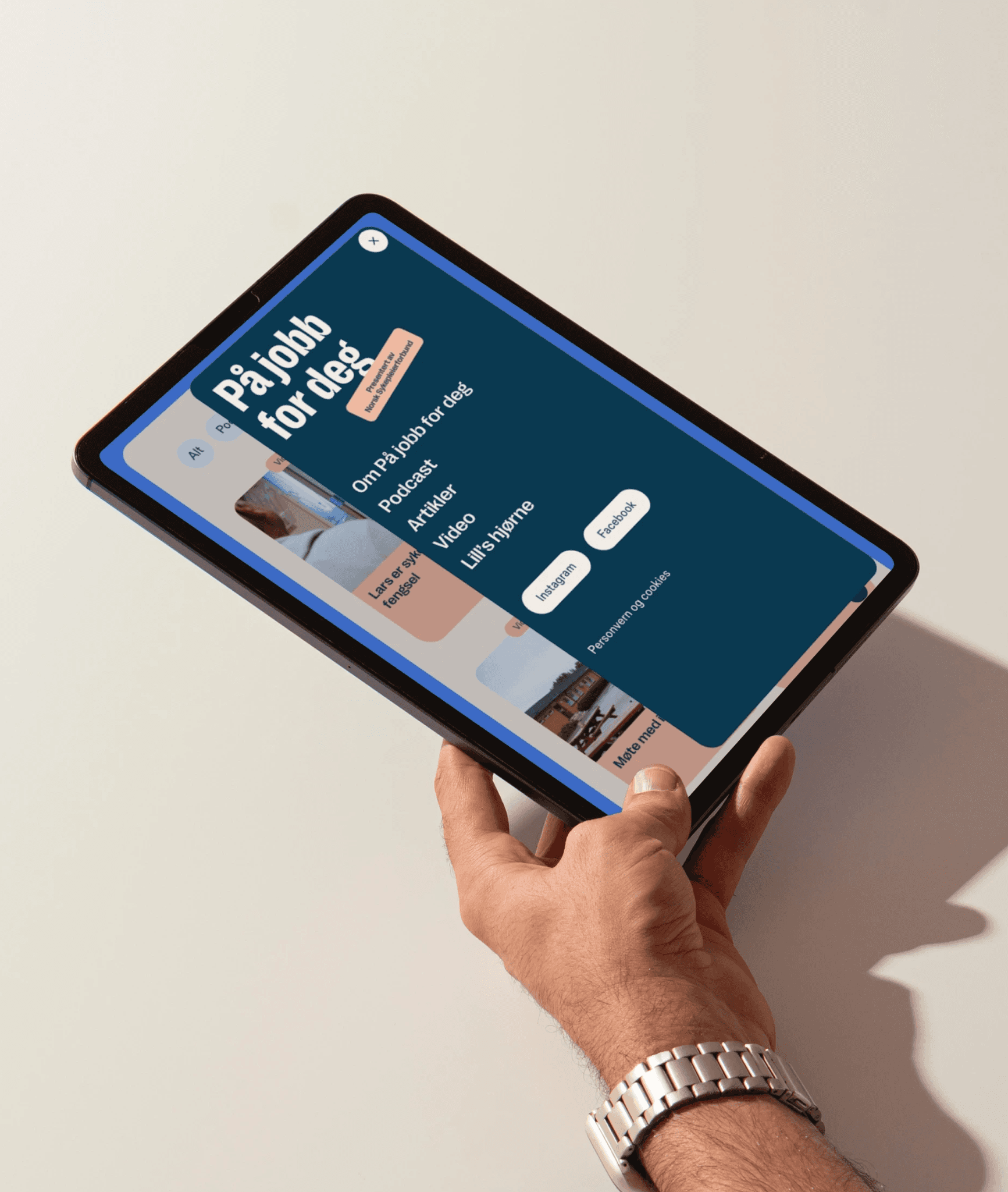 A hand holds an iPad showing the menu desgined for the "På jobb for deg" website.