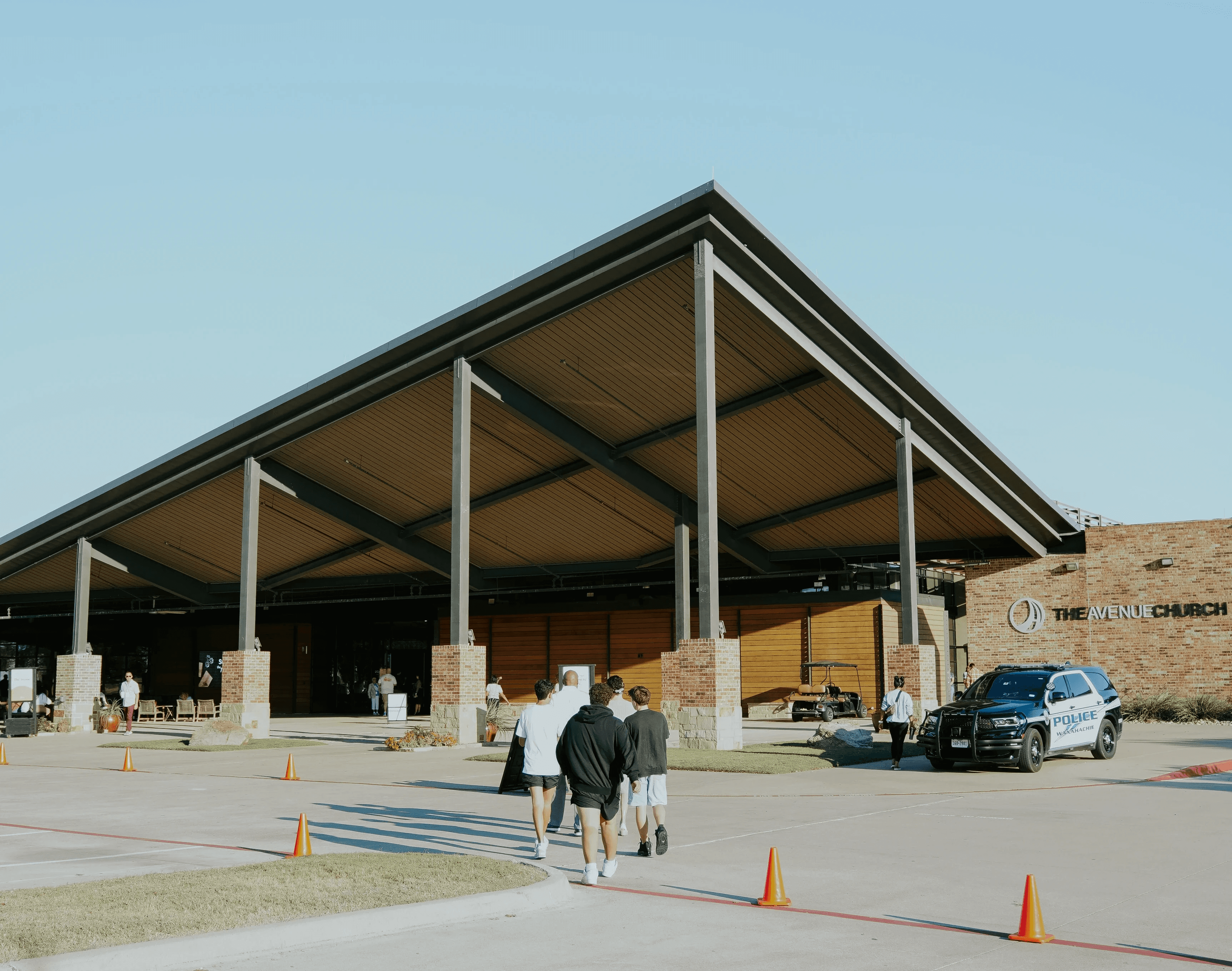 A group of people gather outside a modern building with a wide roof under a clear blue sky.