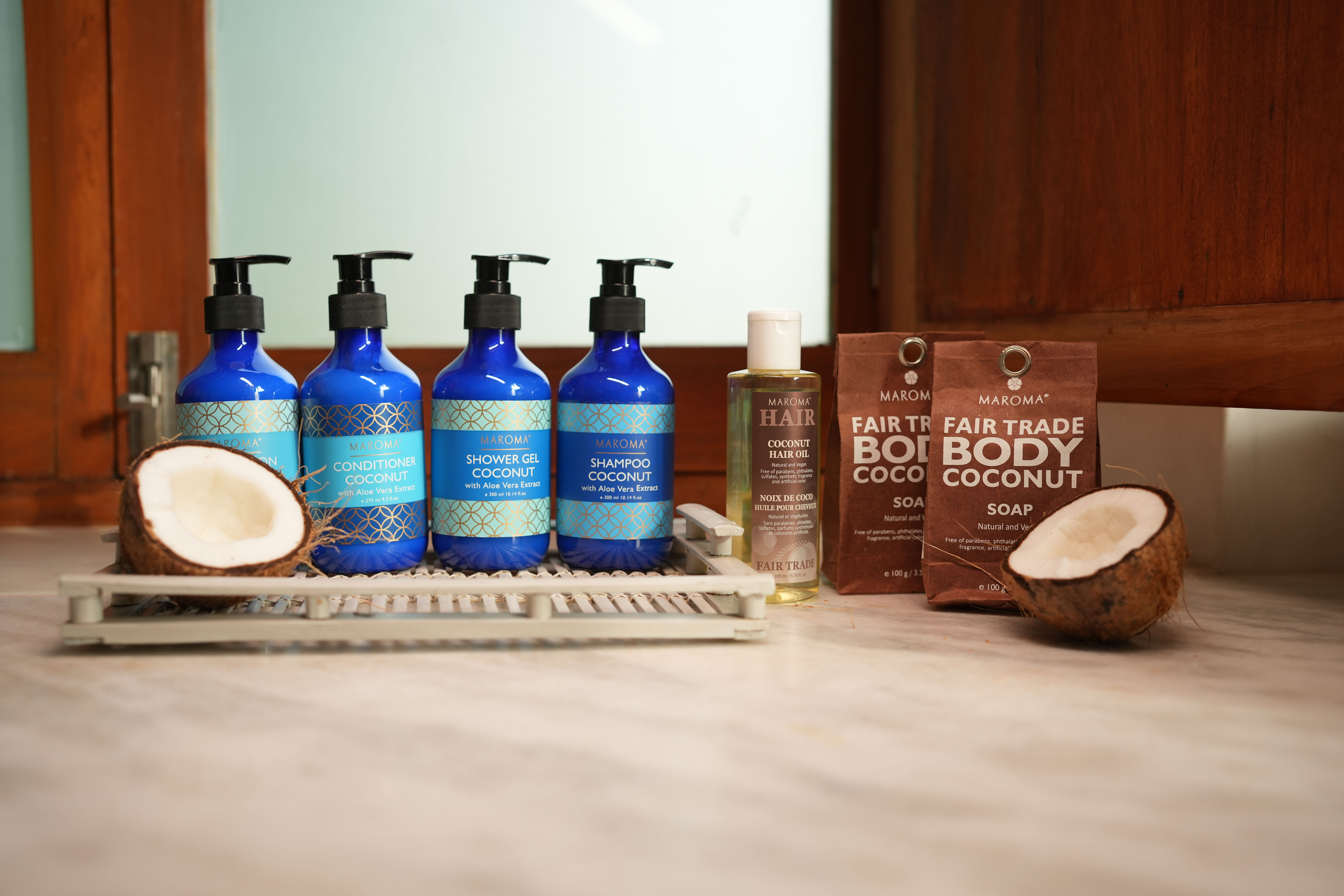 A serene and elegant spa space with wooden reclining chairs and white cushions. Golden sunlight filters through a cascading water feature, creating a peaceful atmosphere. Tropical plants and candles add to the relaxing ambiance.