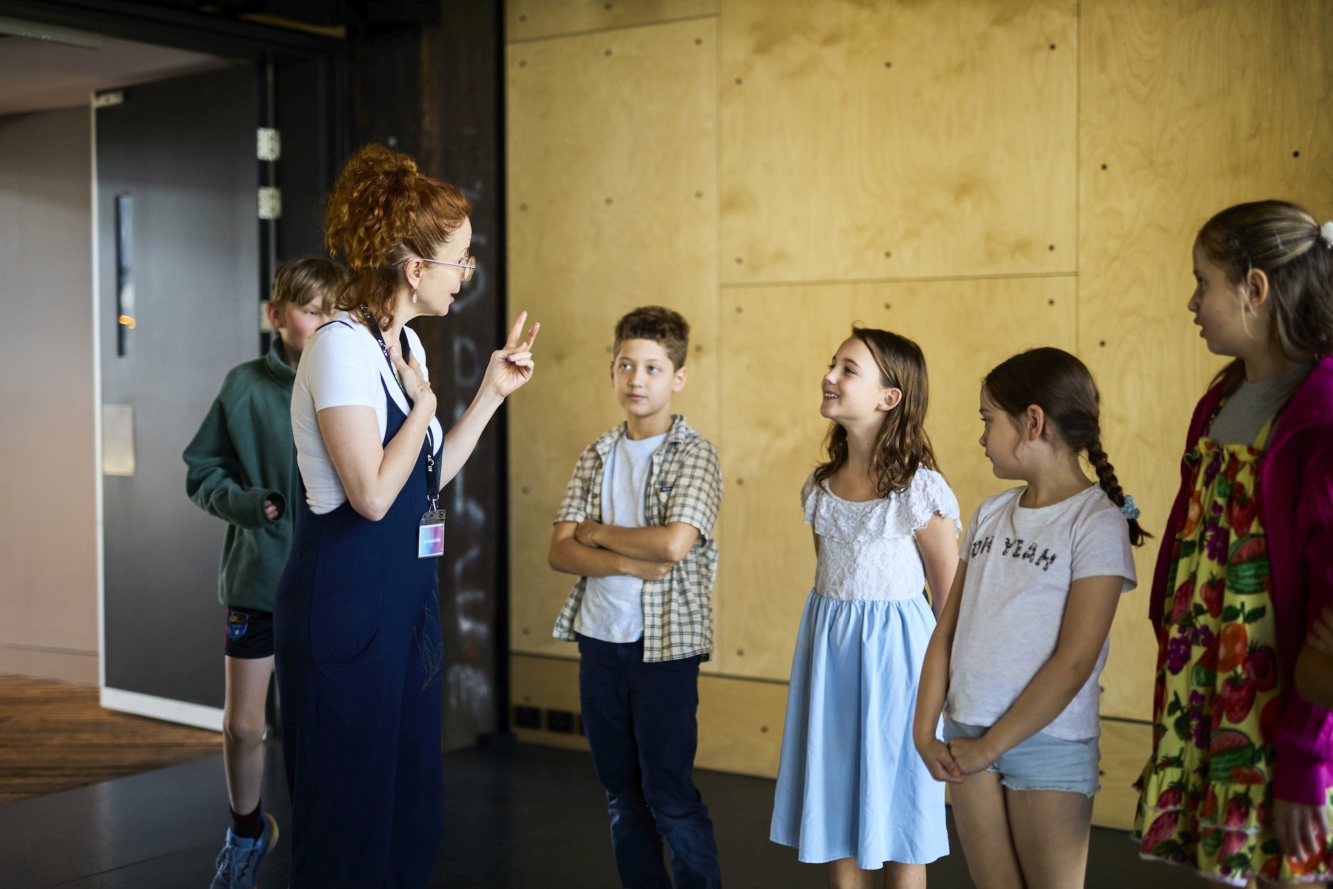 A teaching artist speaks to a group of children standing in a line during a workshop in a studio space.