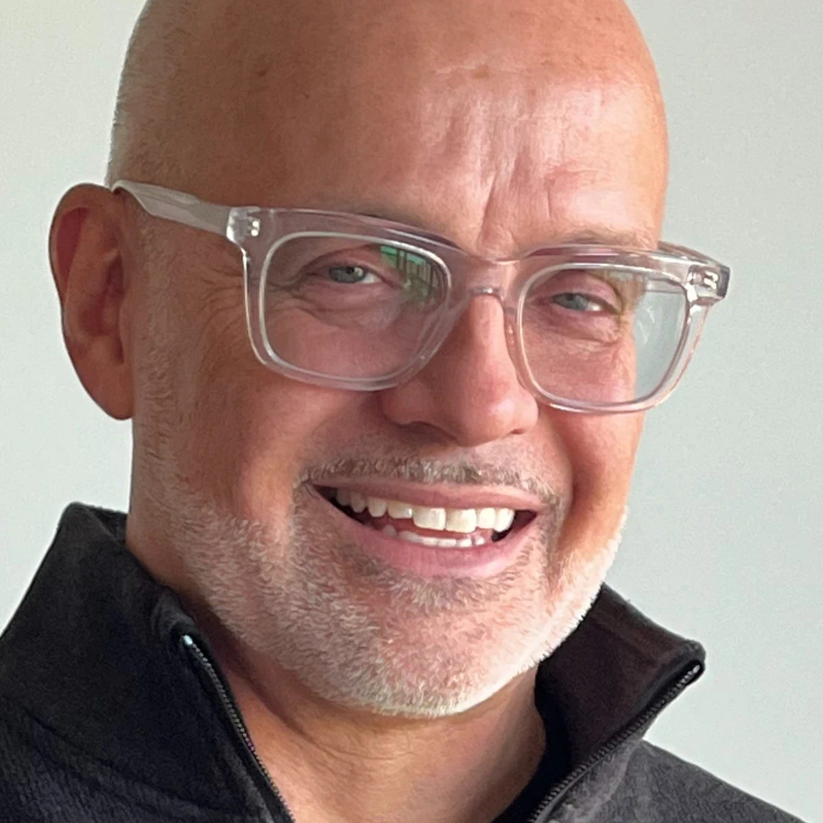 Close-up portrait of Stéphane Paquet smiling at the camera, wearing clear glasses and a dark sweater against a light background.