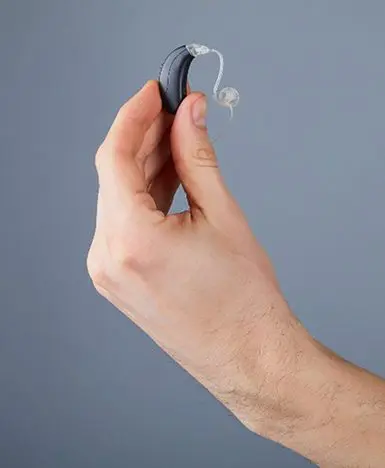 A hand holding a small black object with a looped metal part against a plain gray background.