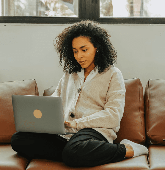 Woman sitting on a sofa using her laptop to book a healthcare appointment through its4women MyClinic.
