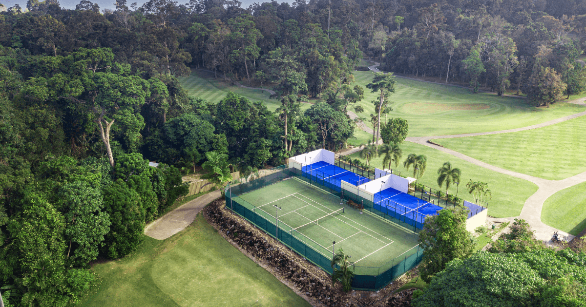 Two outdoor padel courts and a tennis court surrounded by greenery and open fields.