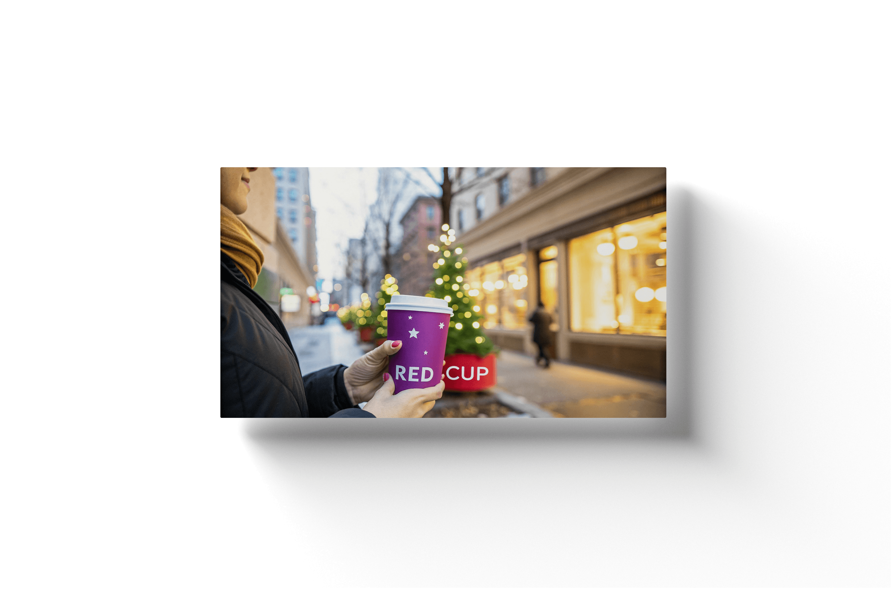 a close up of a woman holding a red cup in front of a christmas tree on a city street