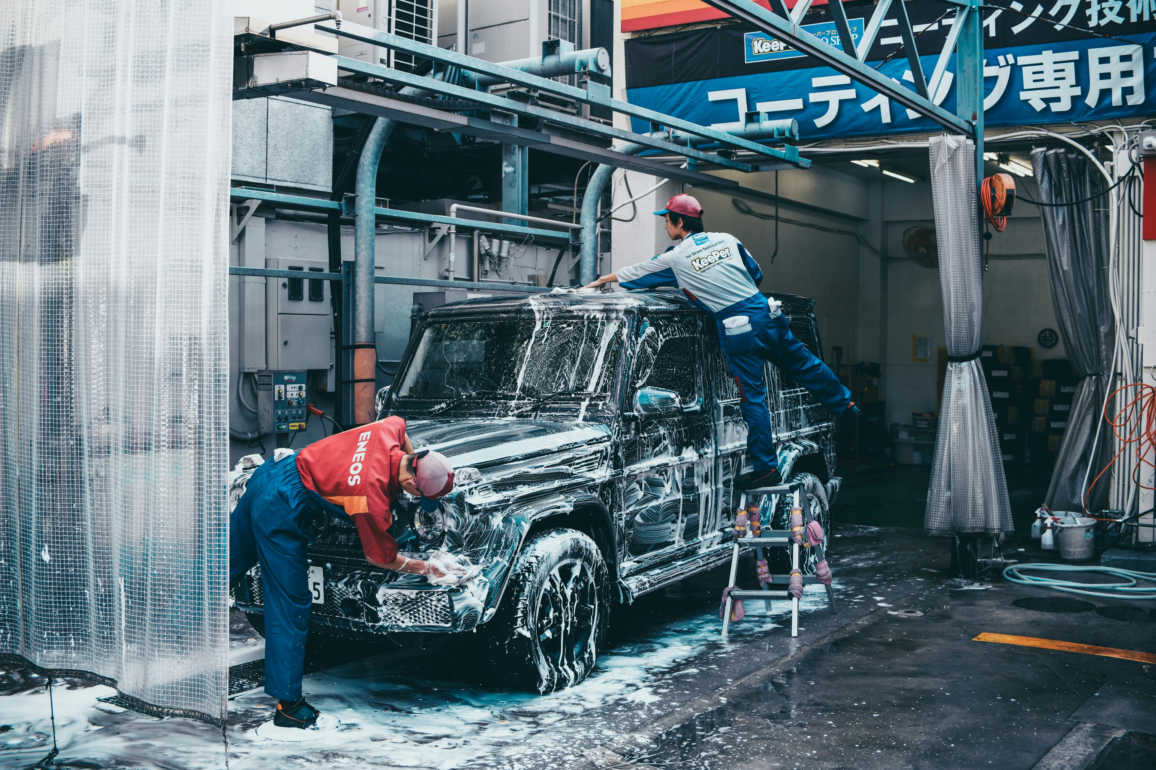 Two men cleaning a vintage car during a carwash one scrubbing the hood, the other working on the roof