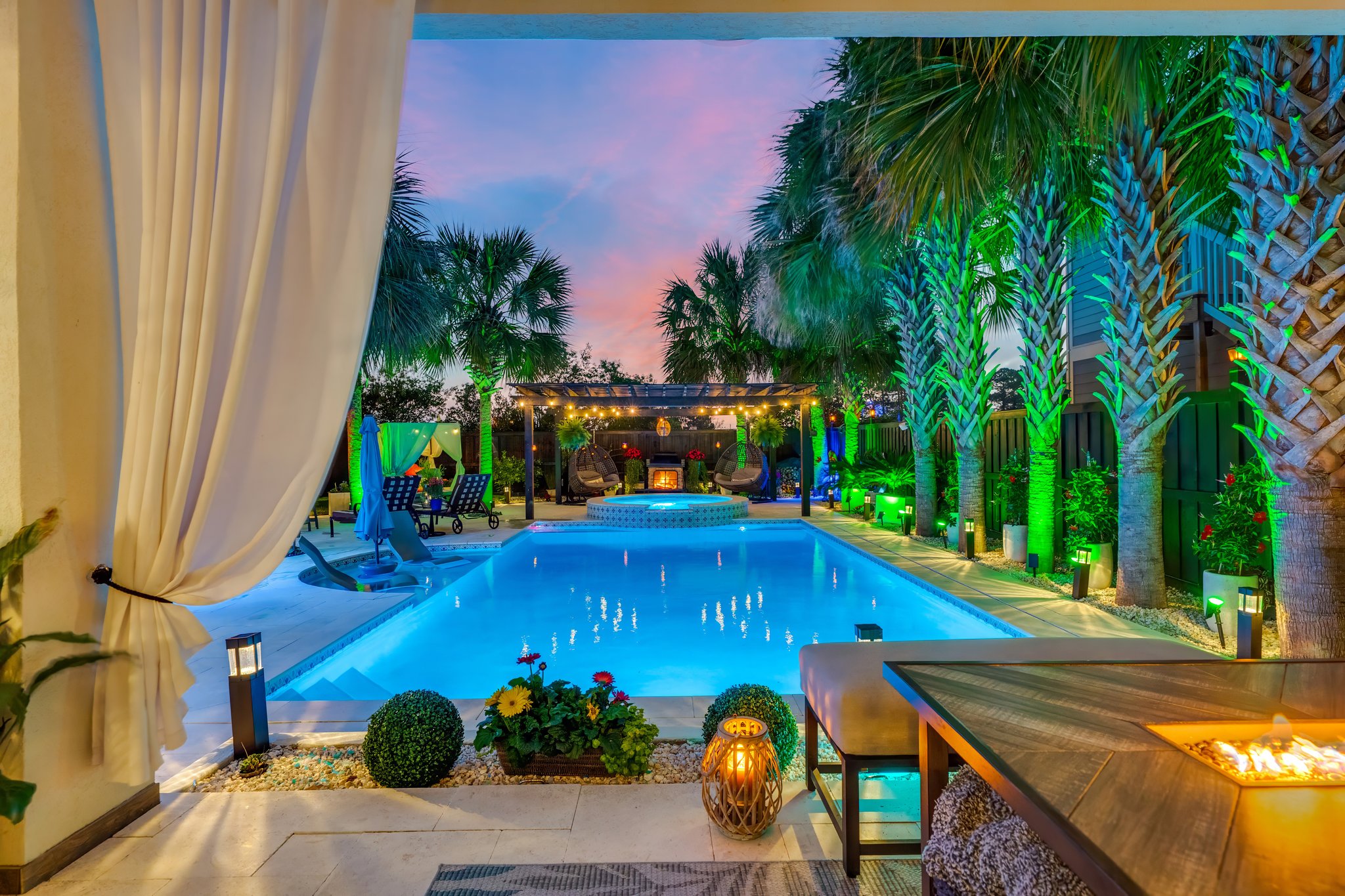 Landscaped courtyard pool at dusk in Panama City Beach, FL, with palms, a pergola and an outdoor fireplace