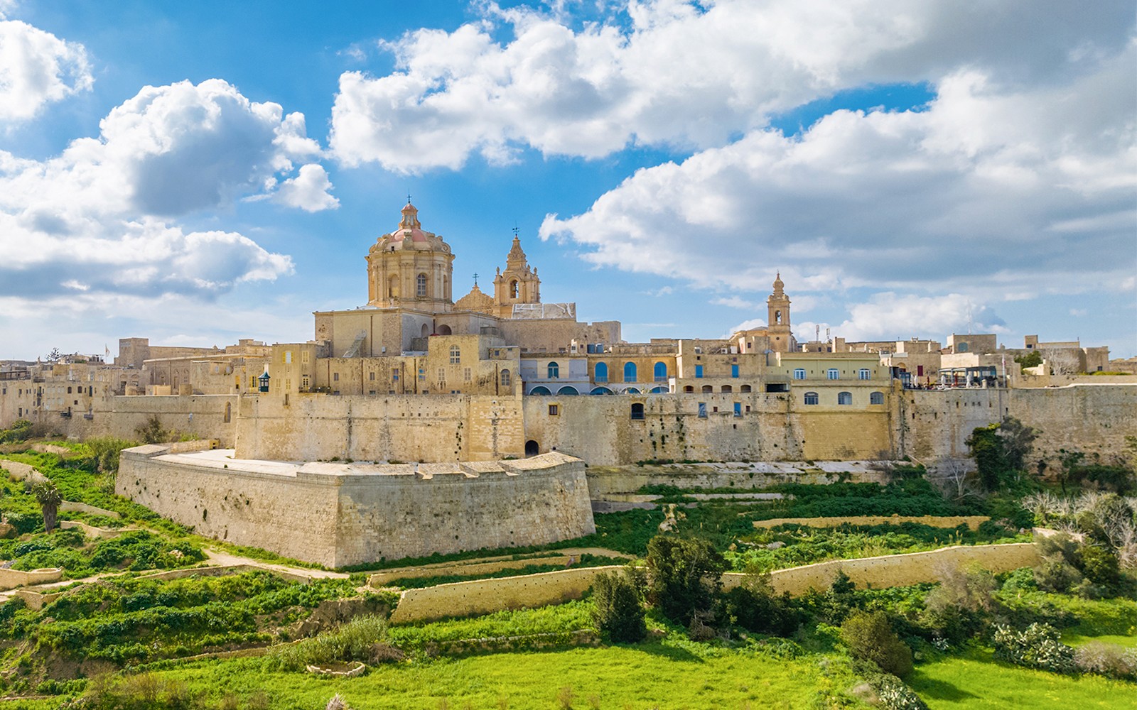 Mdina Gate and city walls in Malta under a blue sky.