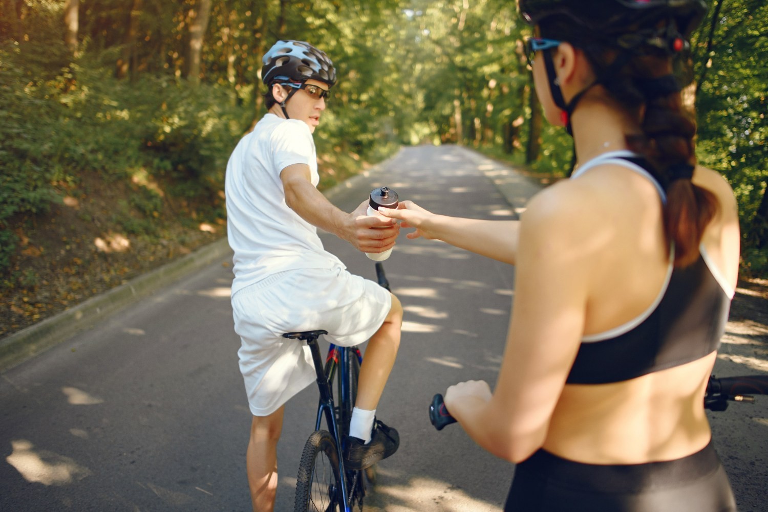 Triathloniści trenujący jazdę na rowerze w przygotowaniach do Ironman 70.3, przekazujący bidon podczas długiego treningu