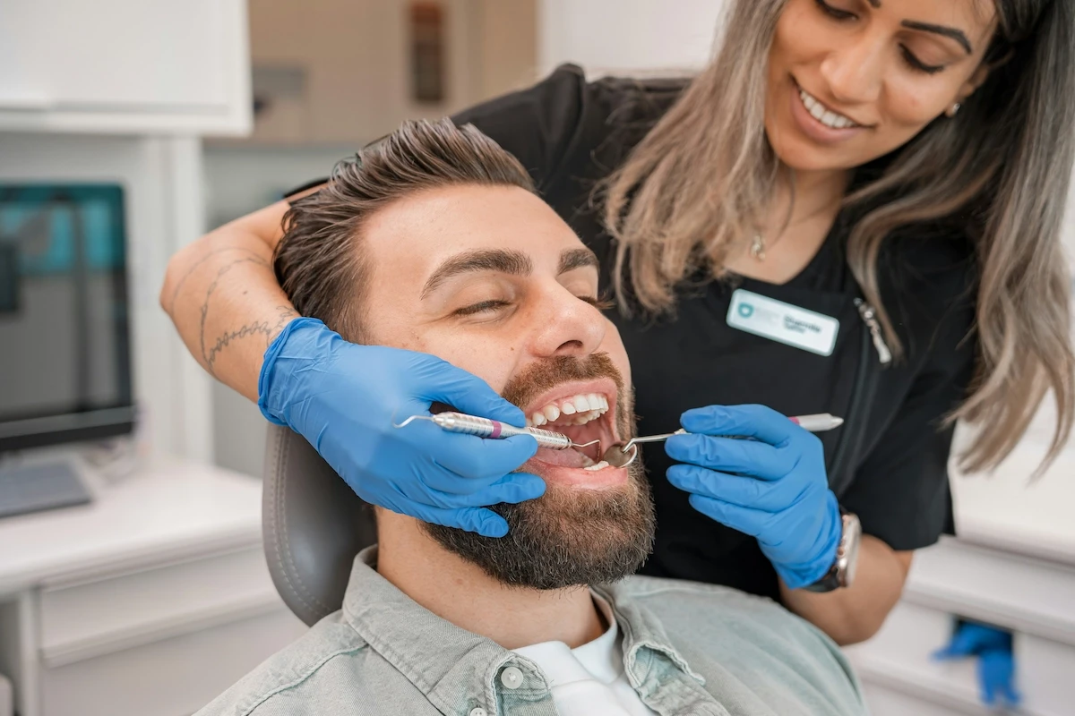 A man is sitting in a chair and a dentist is doing oral hygiene from the side