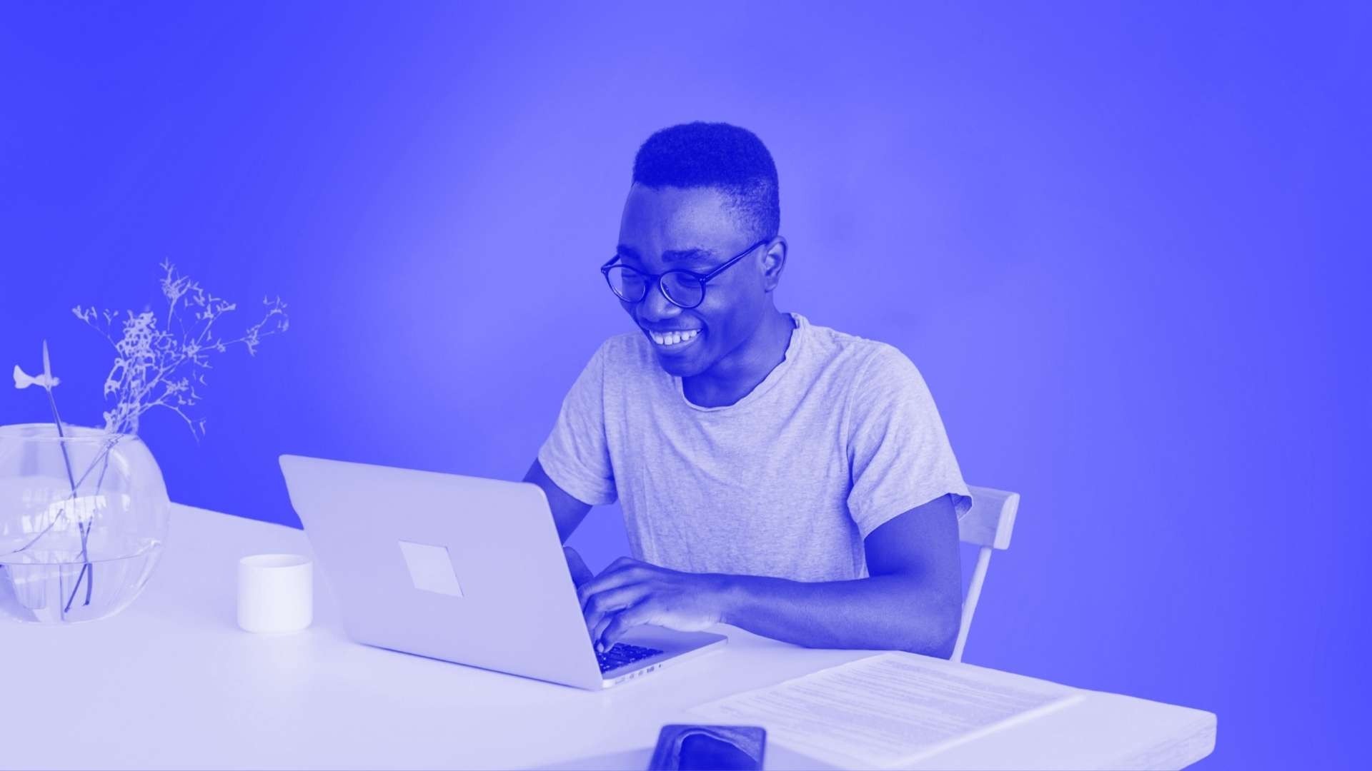 An smiling man wearing glasses typing on his computer while sitting at a desk