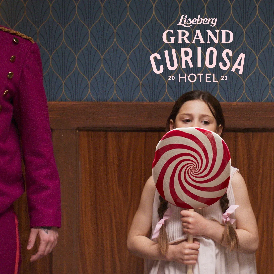 En flicka håller en stor randig klubba framför ansiktet bredvid en piccolo, med texten Liseberg Grand Curiosa Hotel 2023