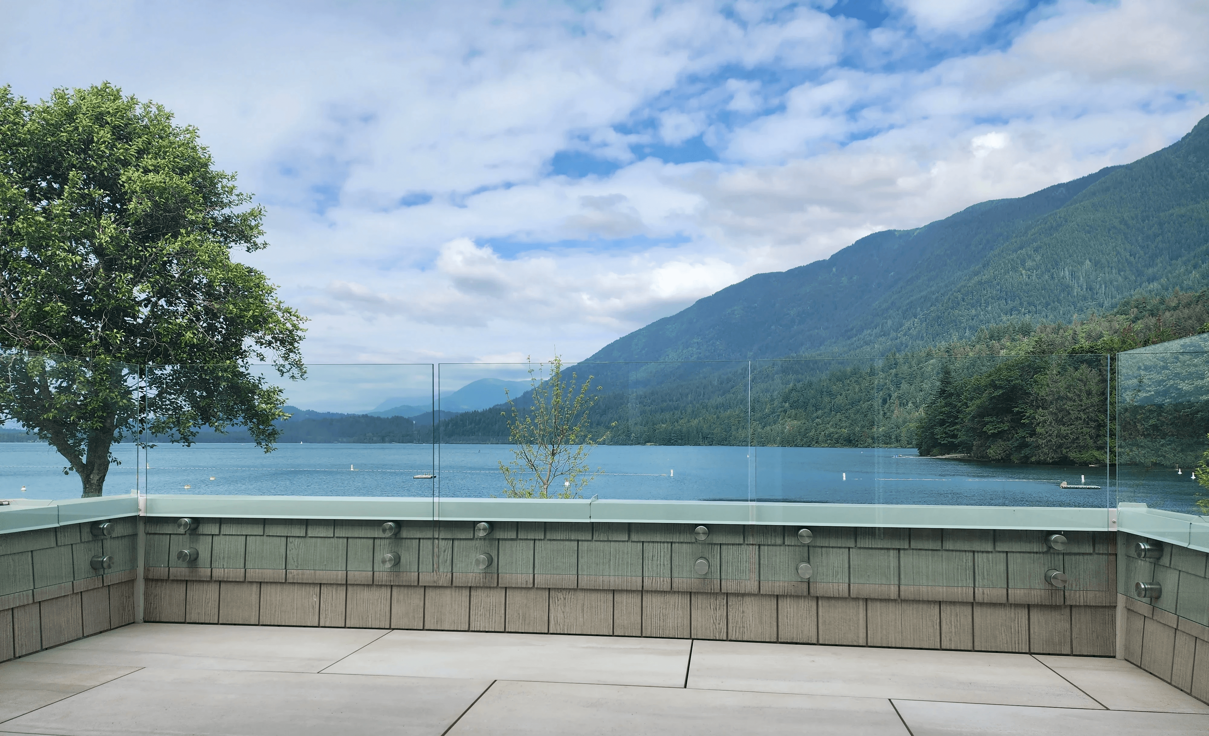 Frameless glass railing on a lakeside patio with panoramic water views, rolling hills, and a bright blue sky.