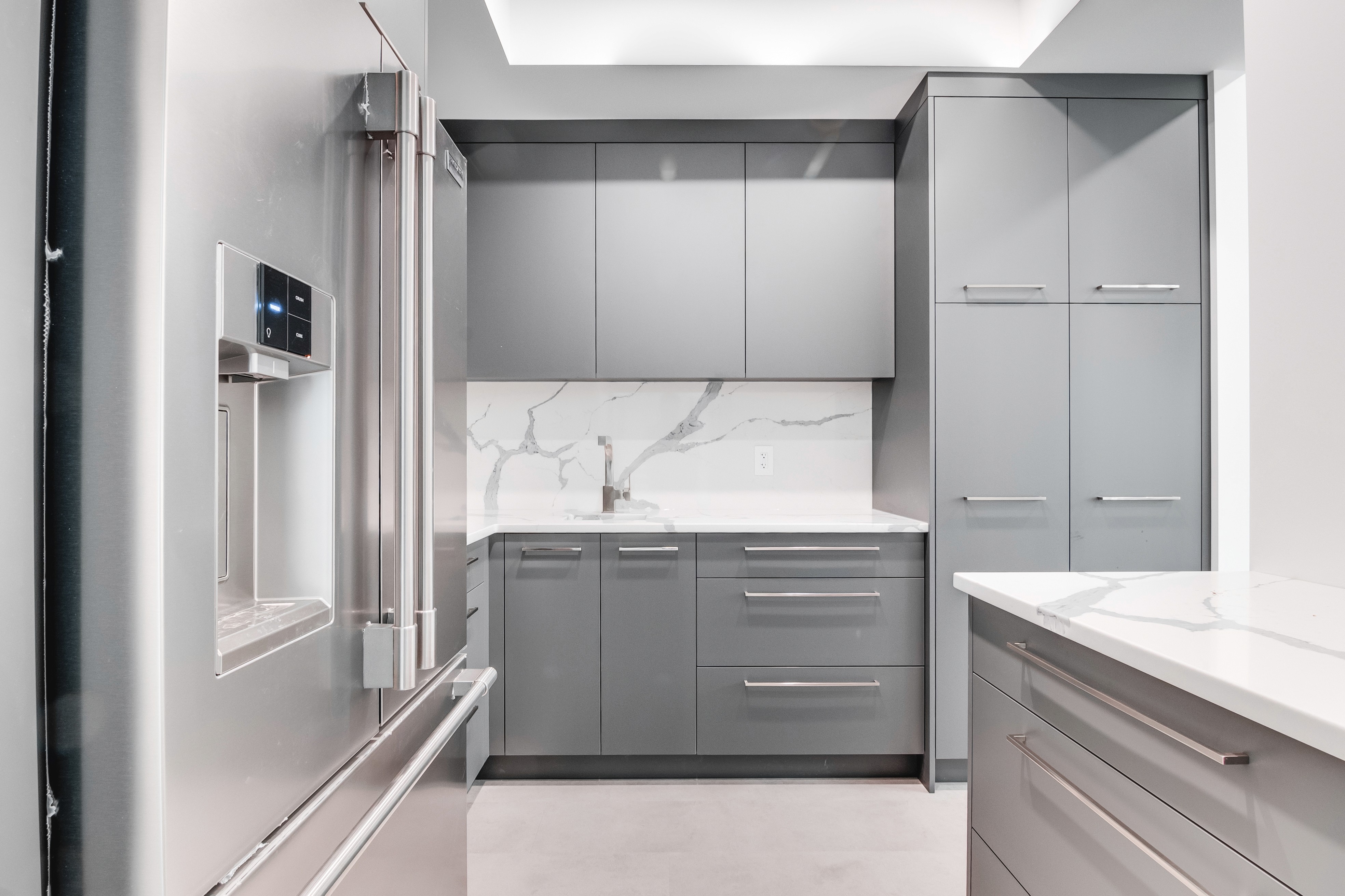 Sleek modern grey kitchen cabinetry with integrated fridge, white countertops, and clean minimalistic design.
