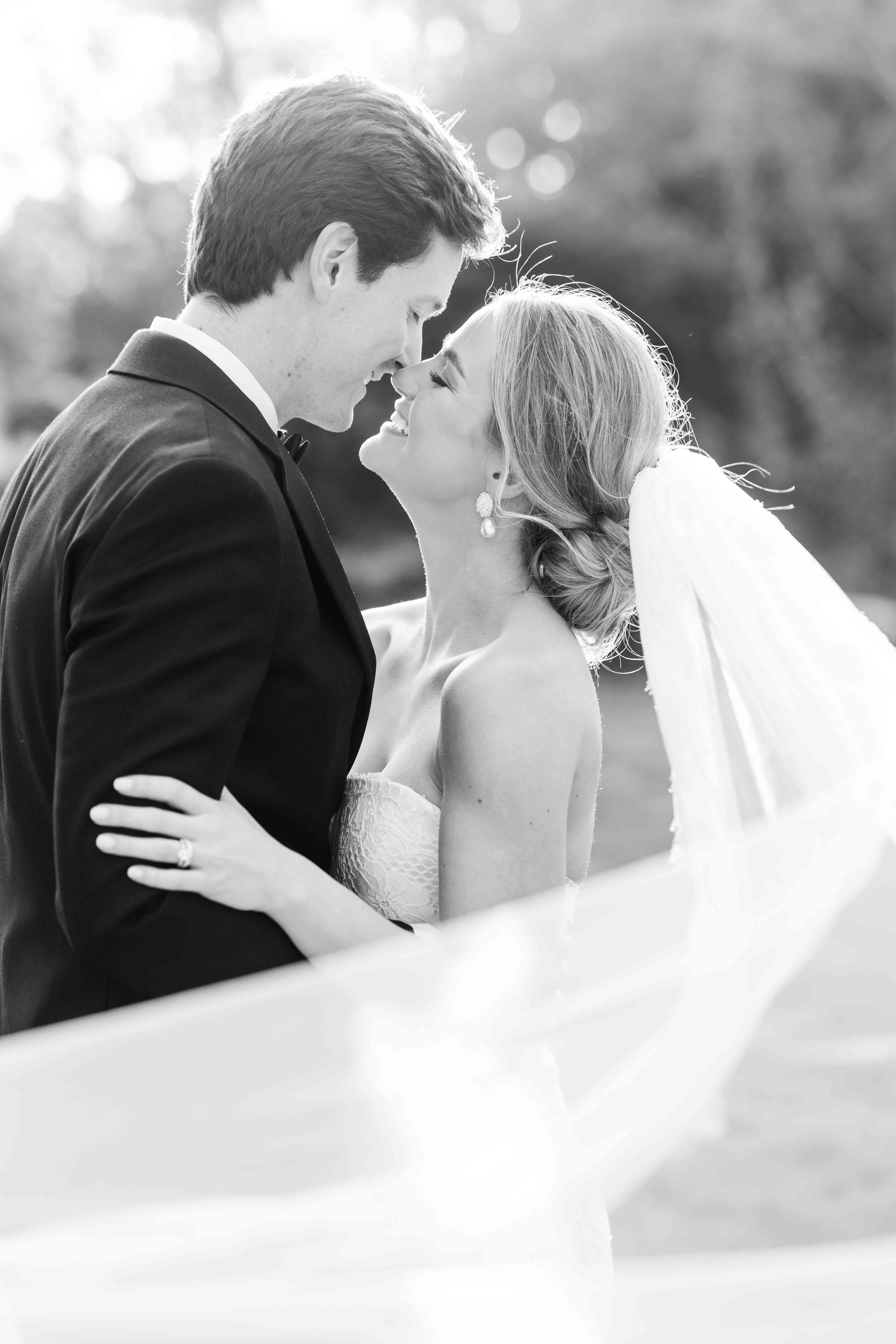 Black and white image of bride and groom kissing with their veil wrapped around them.