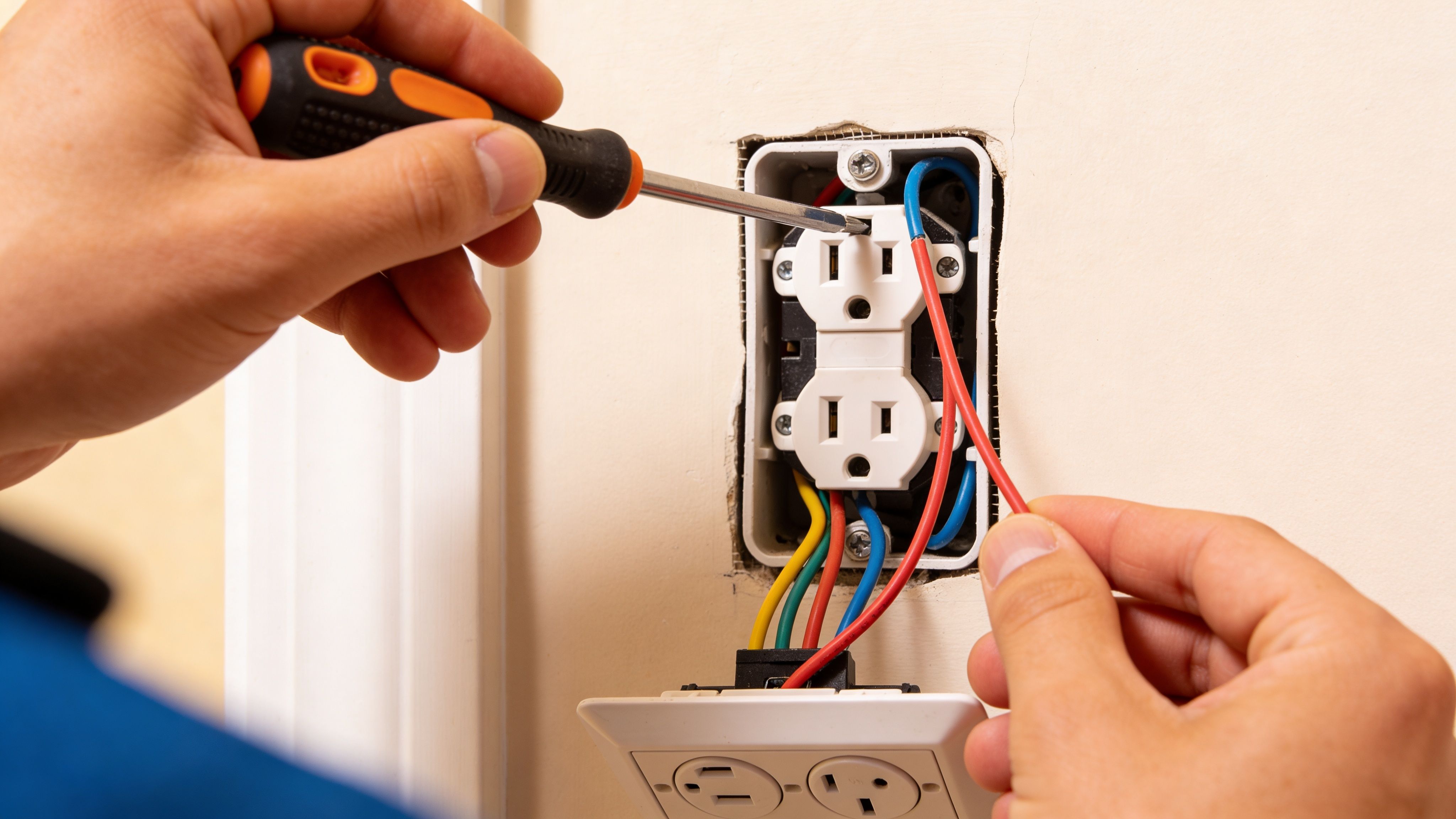 Electrician repairing wall electrical outlet and connecting wiring with screwdriver