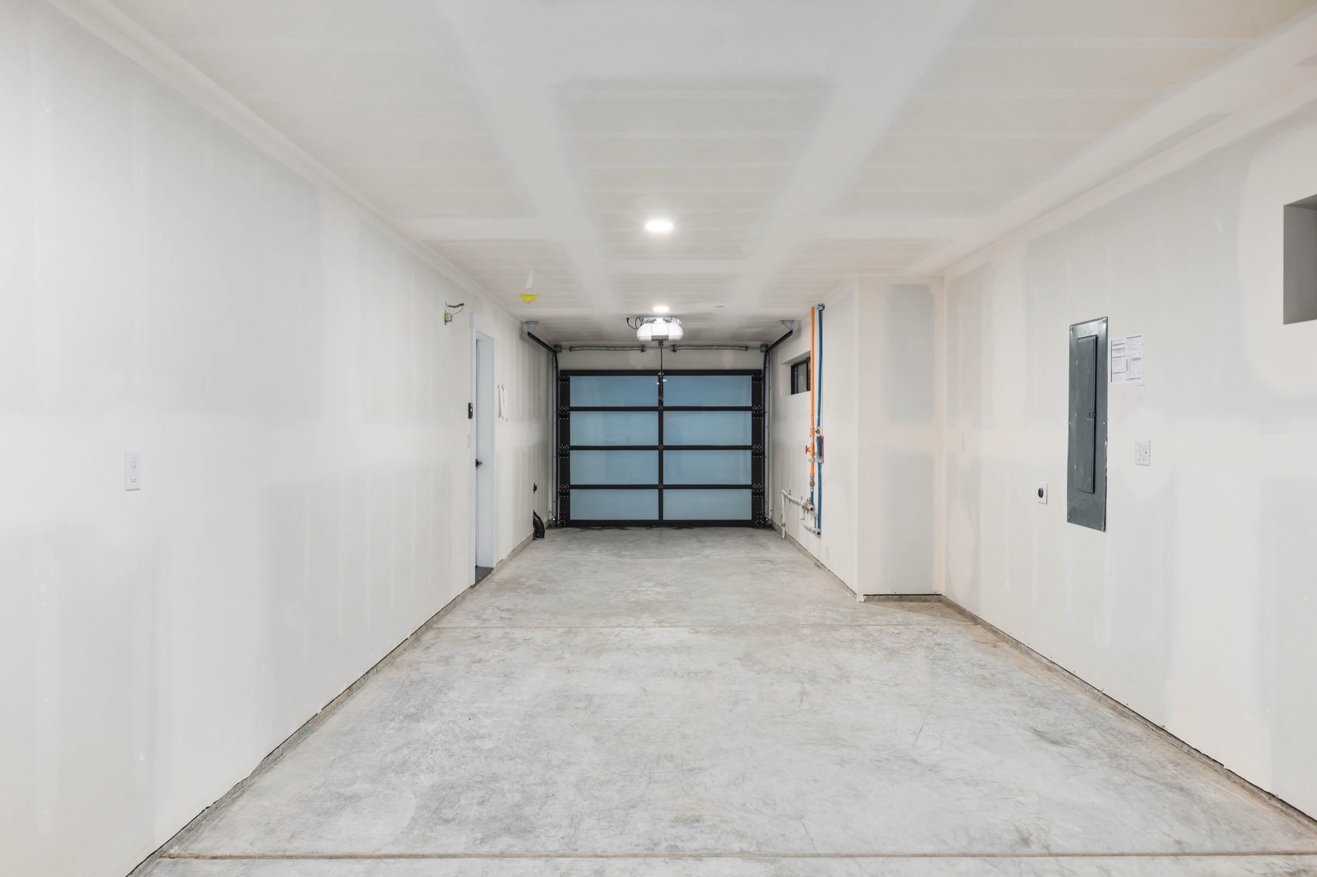 Spacious two-car garage interior in a luxury residential home with glass-panel garage door, recessed lighting, smooth concrete floor, and electrical panel