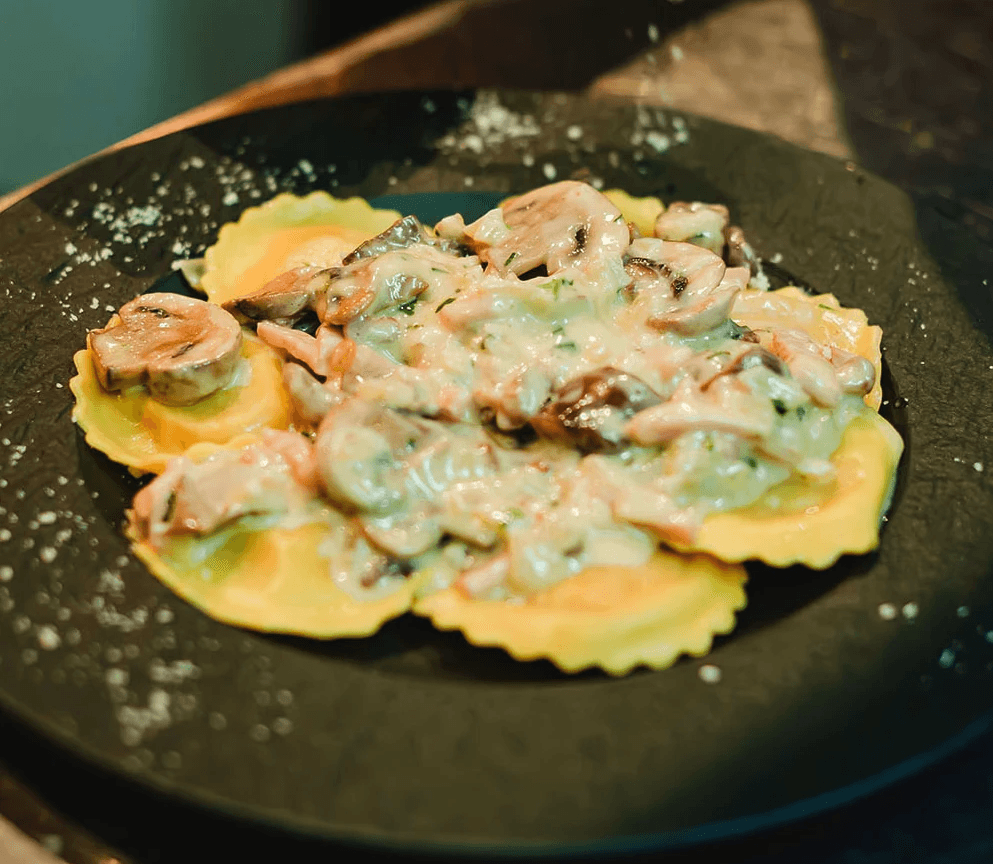 Close-up of fresh ravioli topped with a creamy mushroom sauce, served on a dark plate.